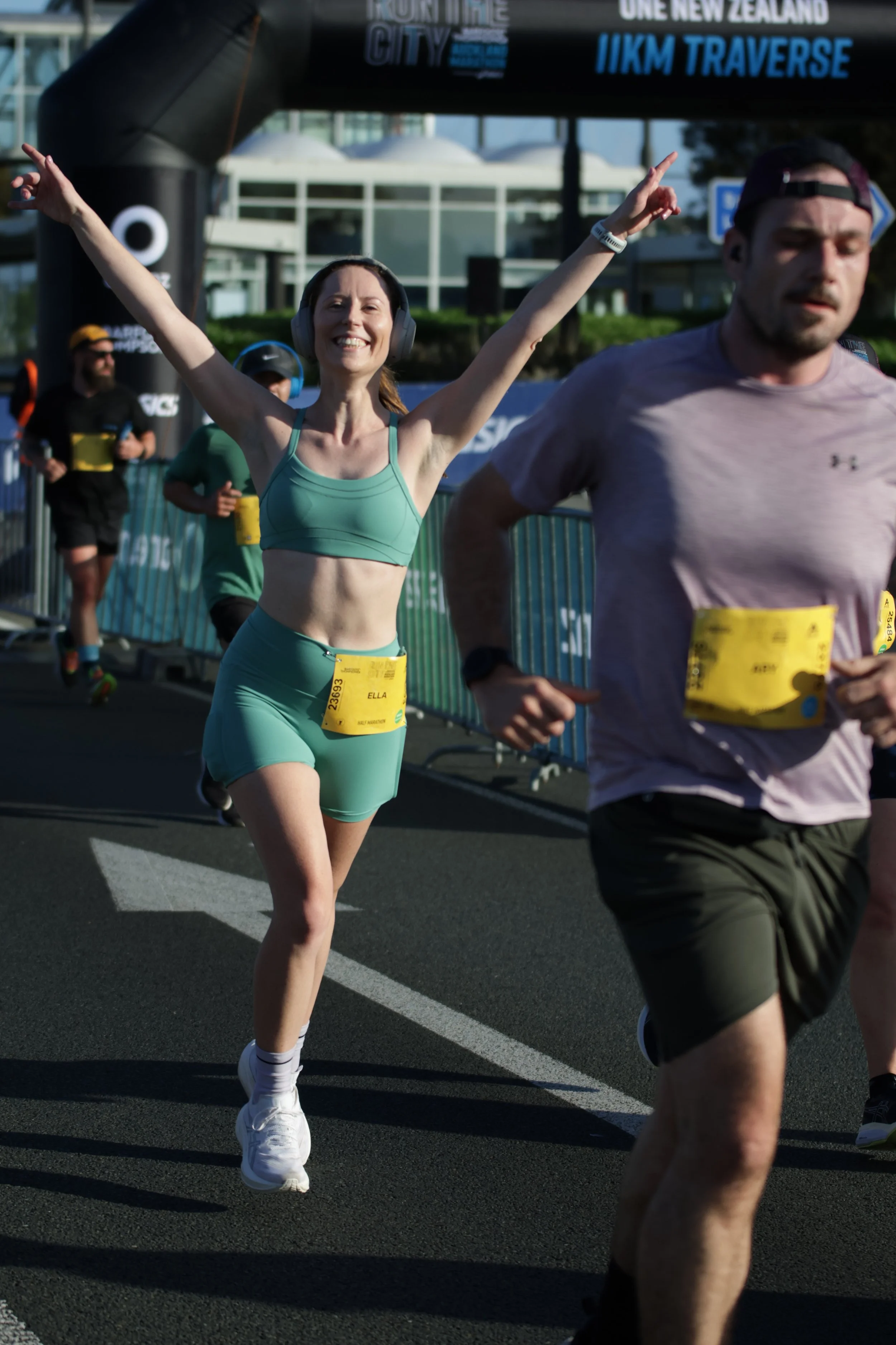 People running in a marathon, with a woman smiling and raising her arms as she approaches the finish line, which is marked with an archway.