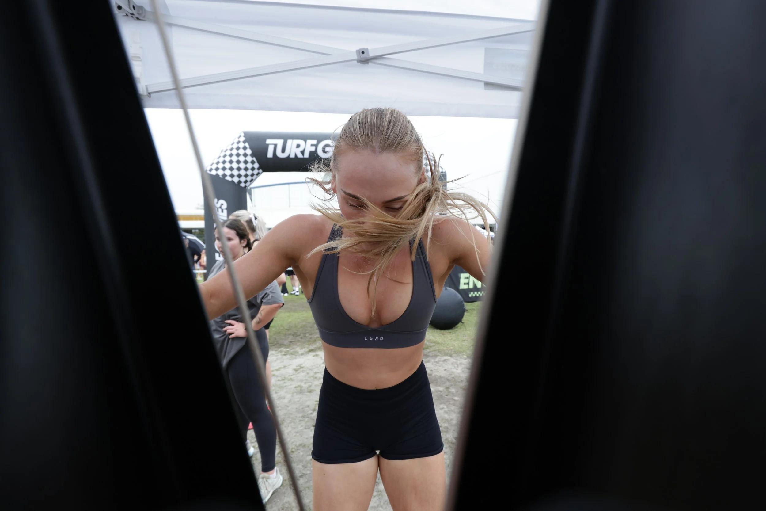 A woman in athletic wear is leaning forward, with her hair blowing across her face, seen through the spokes of a bicycle wheel at a racing event.