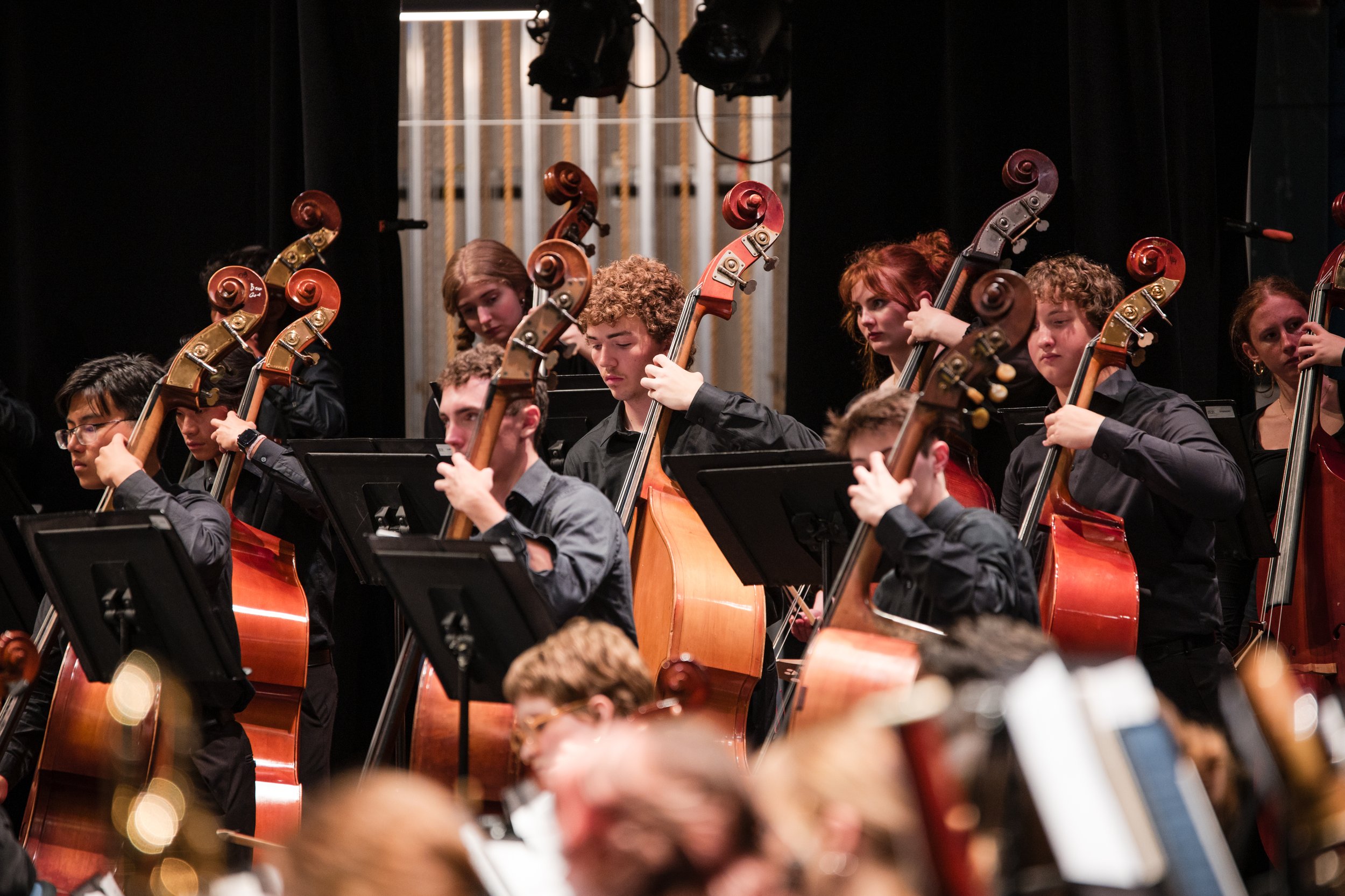 Young musicians playing cellos in an orchestra on stage.