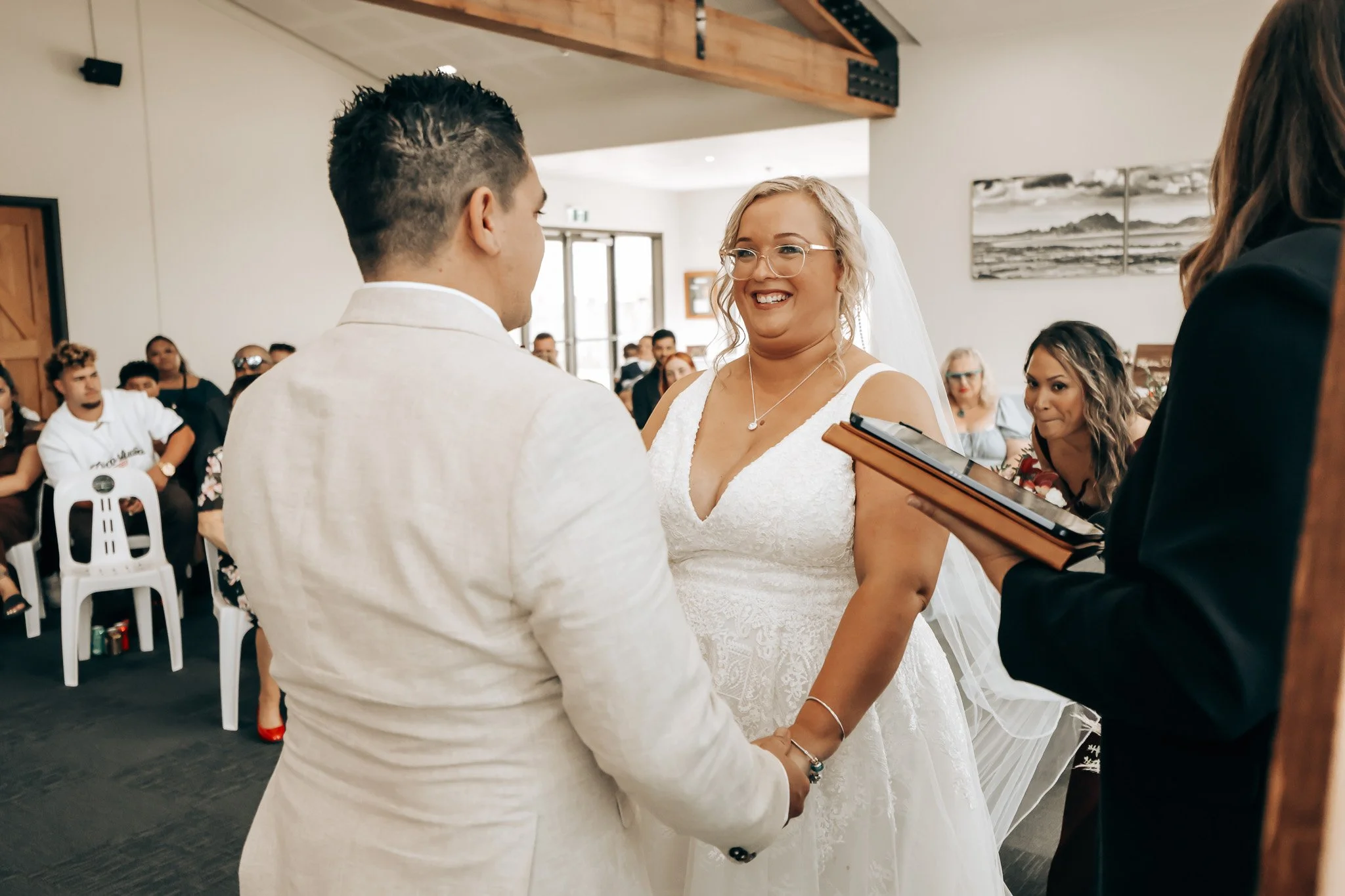 A bride and groom exchanging vows during a wedding ceremony indoors, surrounded by guests.