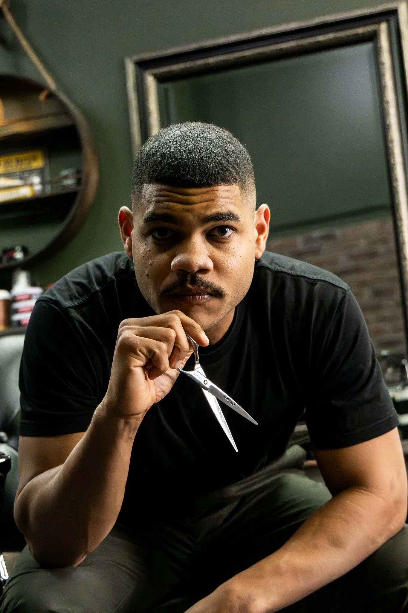 A young man with a fresh haircut holding a pair of scissors in a barbershop.