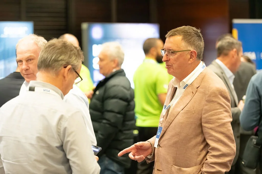 Group of men at a professional conference, engaging in conversation and looking at mobile devices.