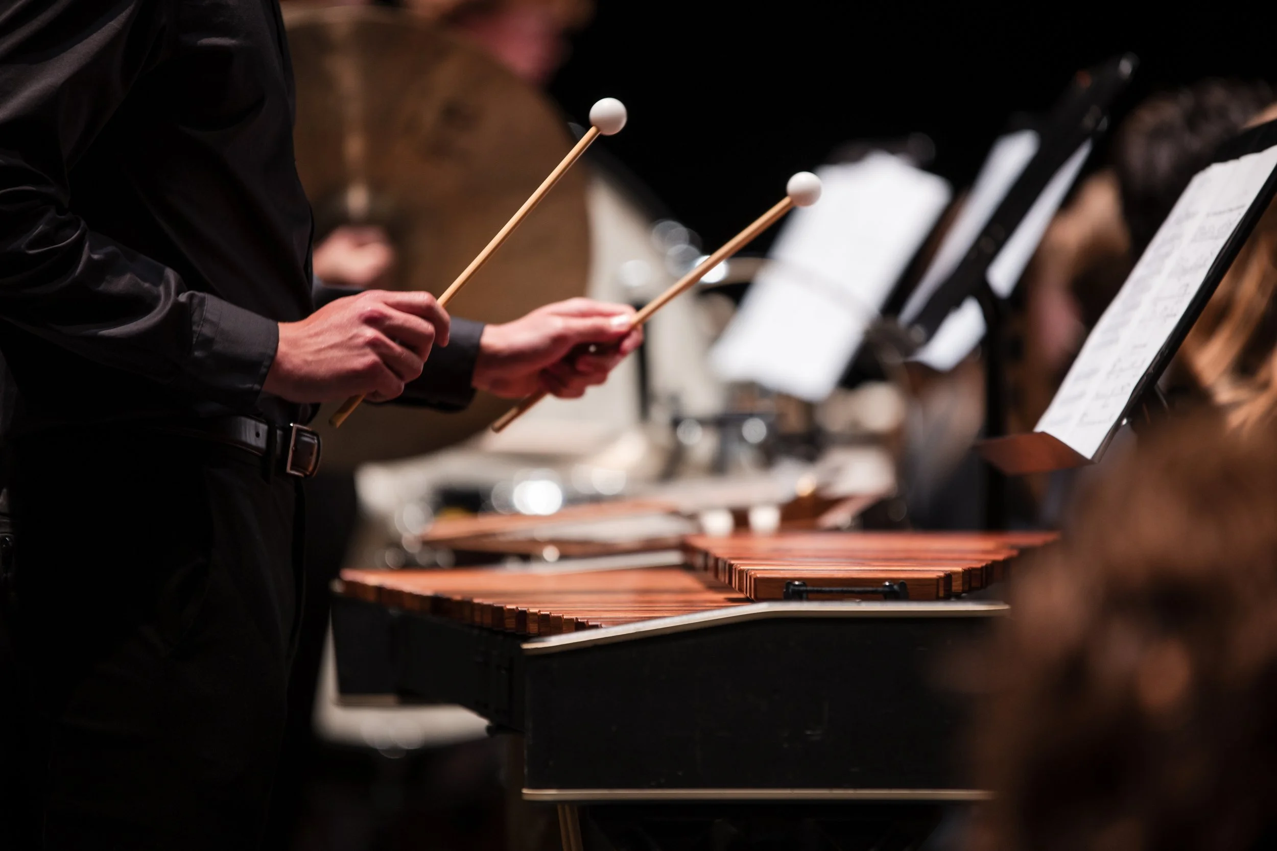 People playing marimbas in an orchestra with music stands and sheet music.