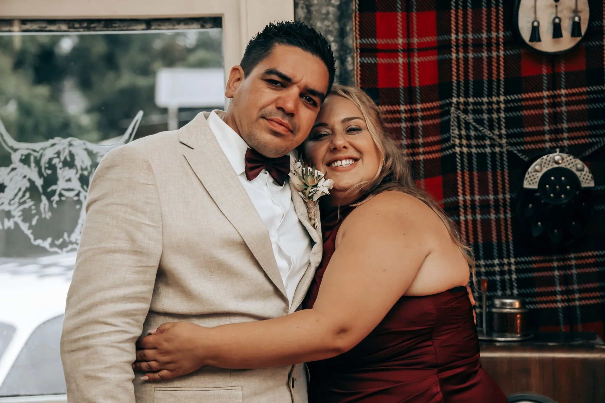 A man and woman embrace in a cozy, vintage-style setting with red plaid decor and a retro telephone on the wall.