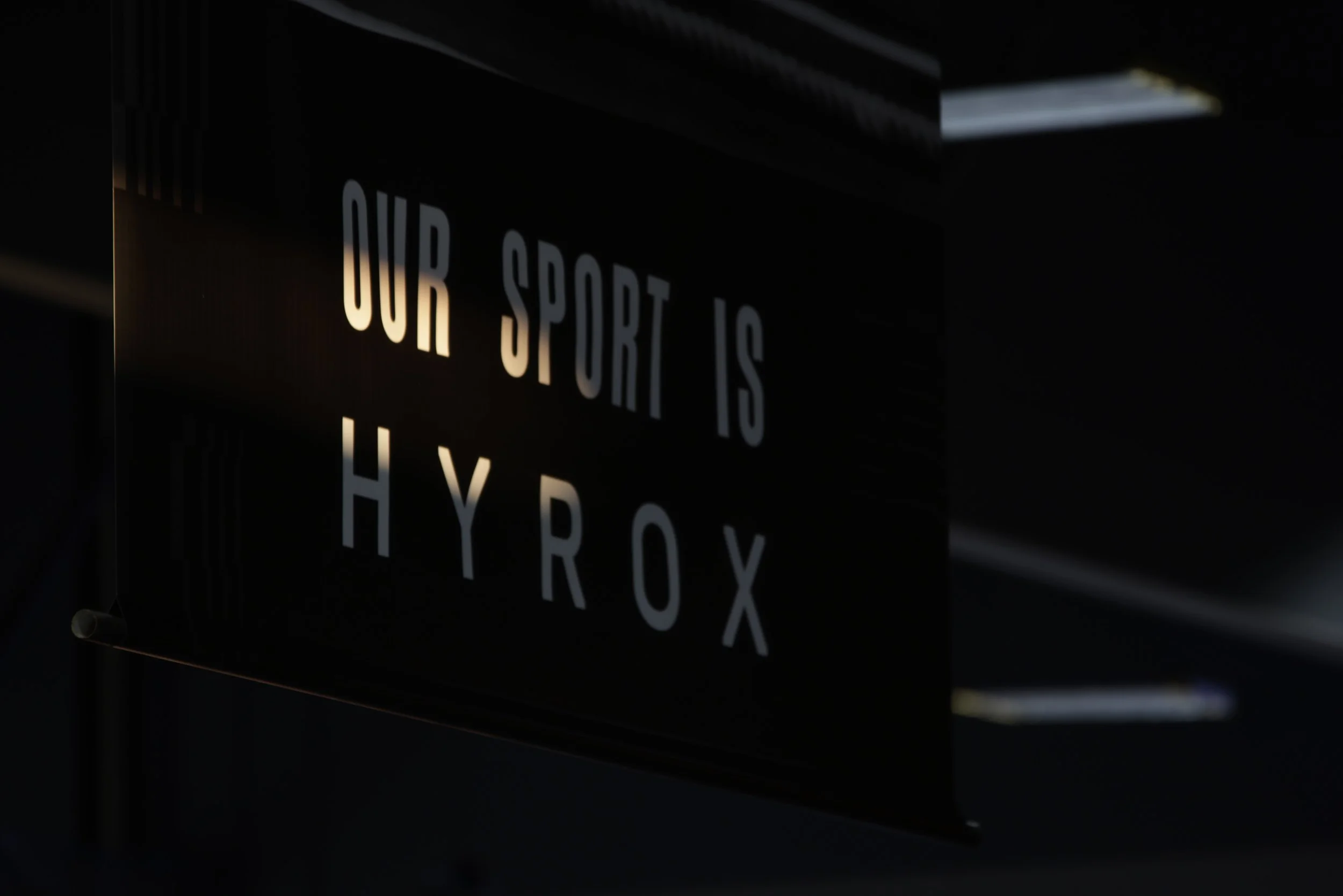 Close-up of a black sign with white letters reading 'OUR SPORT IS' in a dimly lit setting.