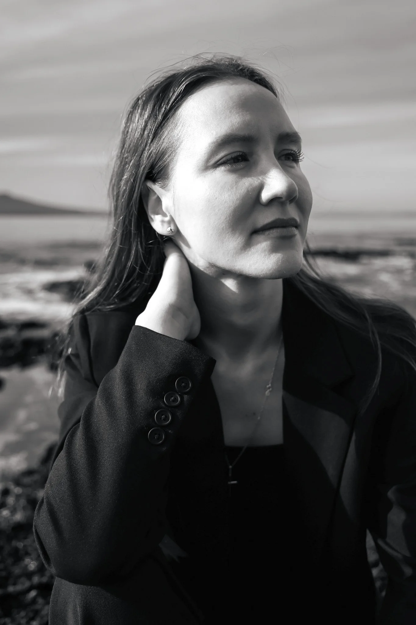 A black and white photo of a woman outdoors with her hand behind her neck, gazing into the distance.