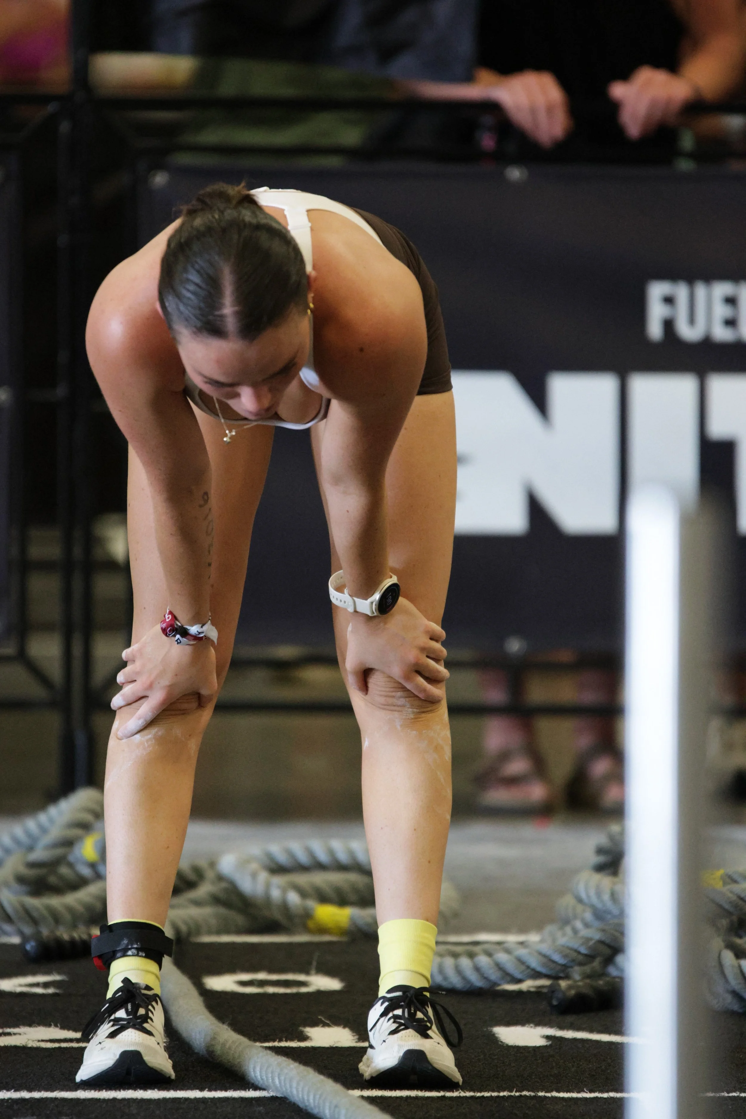 A woman in workout attire bending over during a fitness session, with ropes on the floor and a black background featuring partially visible text.