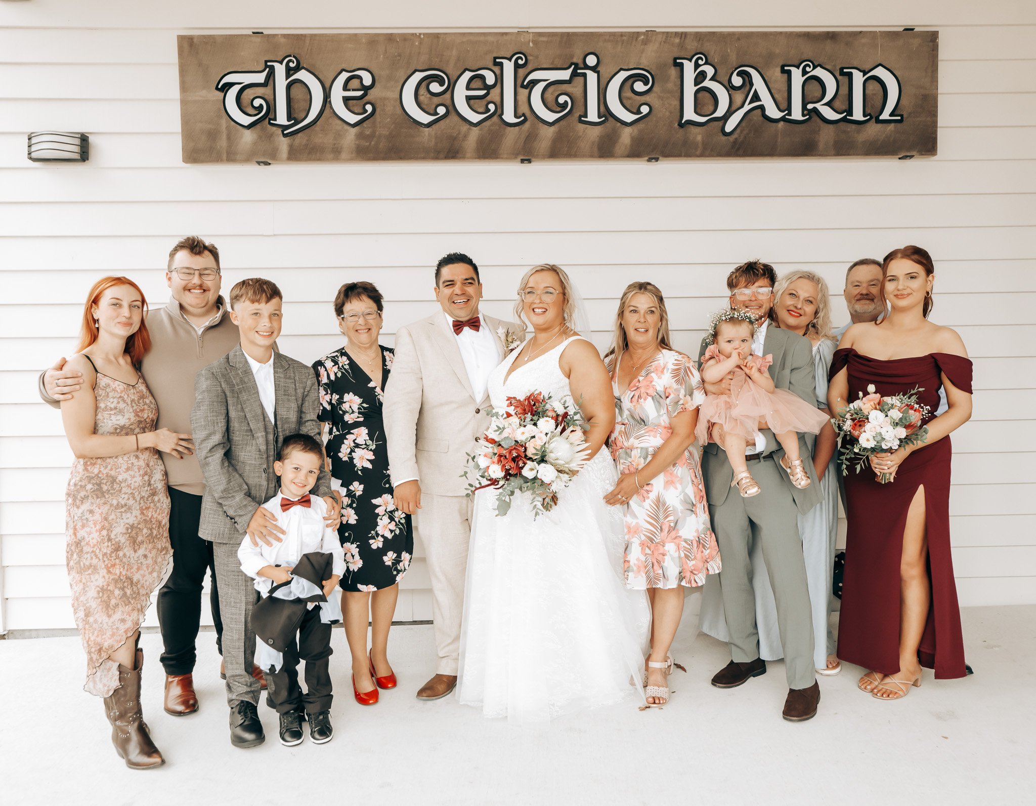 Group of people at a wedding celebration standing in front of a sign that reads 'the Celtic barn'.