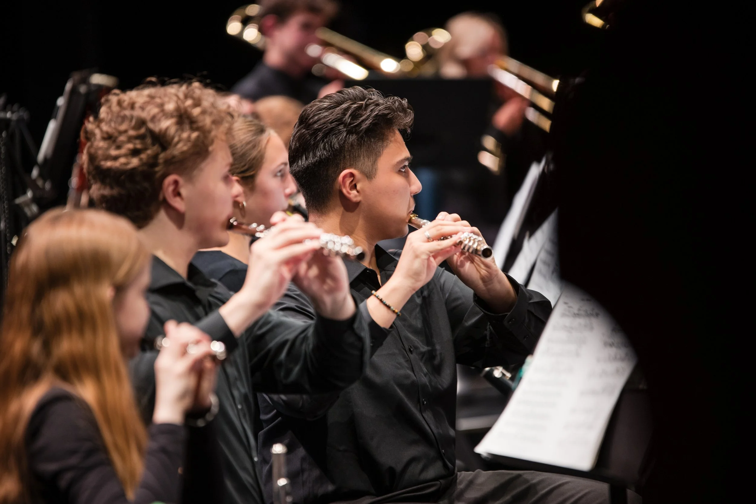 Youth orchestra members playing flutes during a concert.