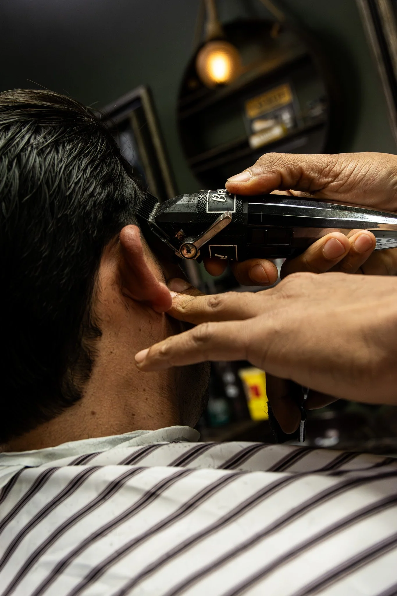 A person receiving a haircut with clippers, while someone else holds the person's head steady. The person getting the haircut is wearing a striped shirt.