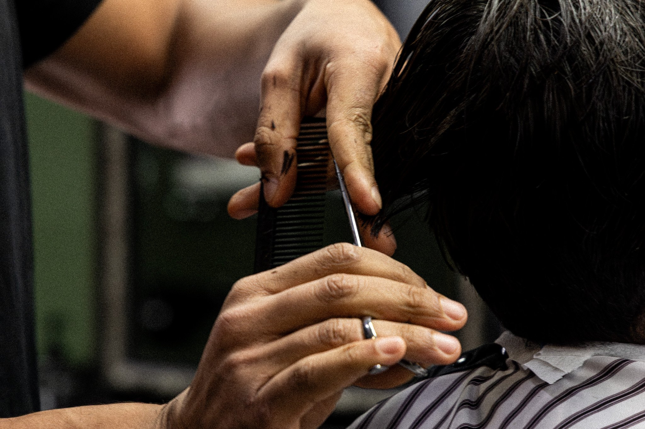 A person trimming their dark hair with scissors while holding a comb.
