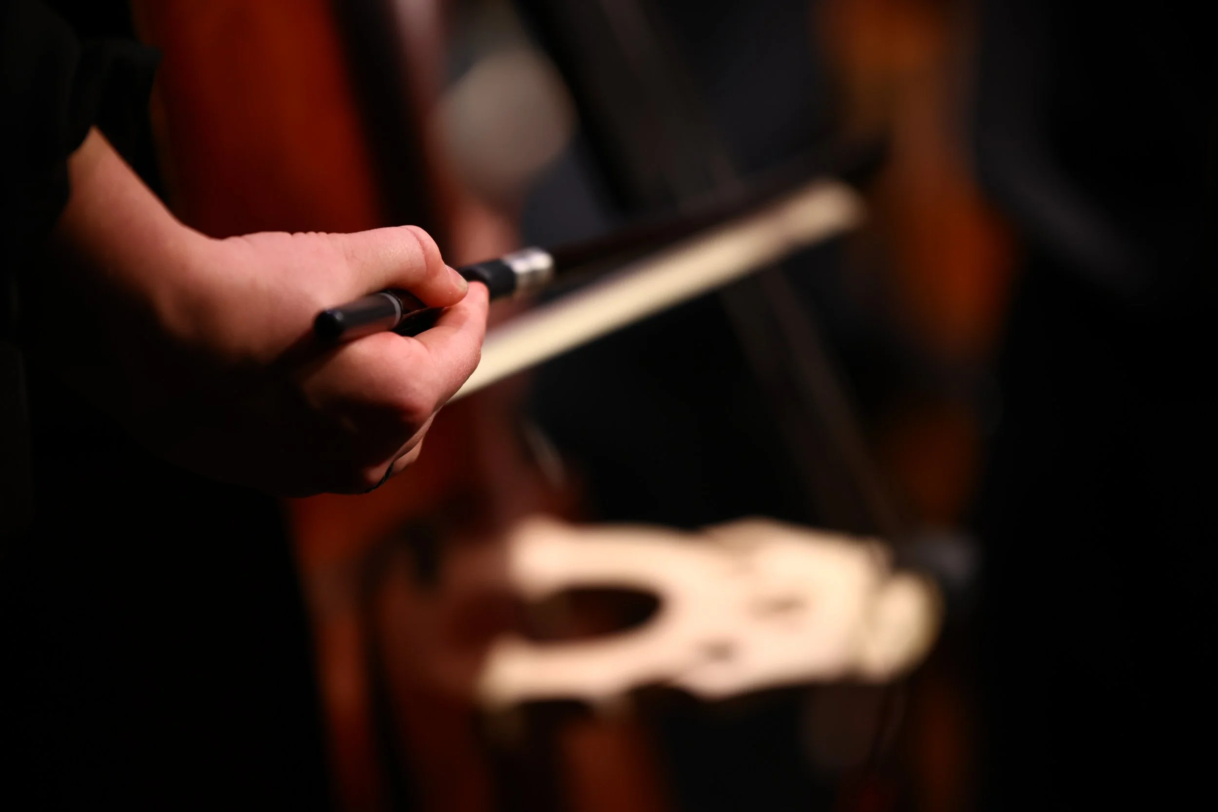 Close-up of a person's hand holding a black pen, with a blurred background of a musical piano keyboard.