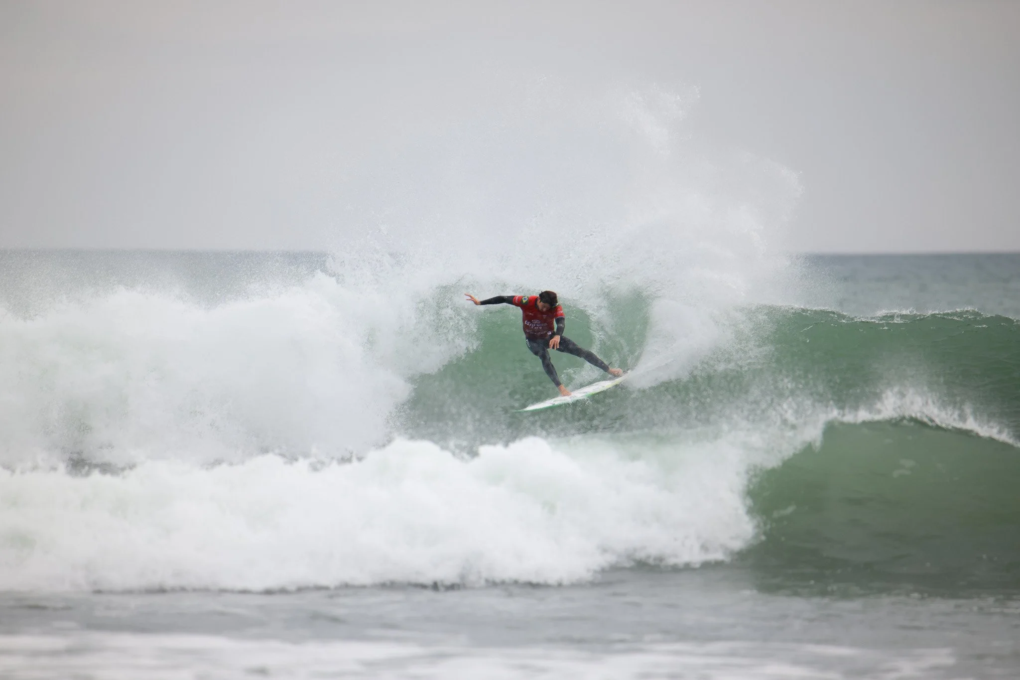 A person surfing on a wave in the ocean, wearing a rash guard and black wetsuit.