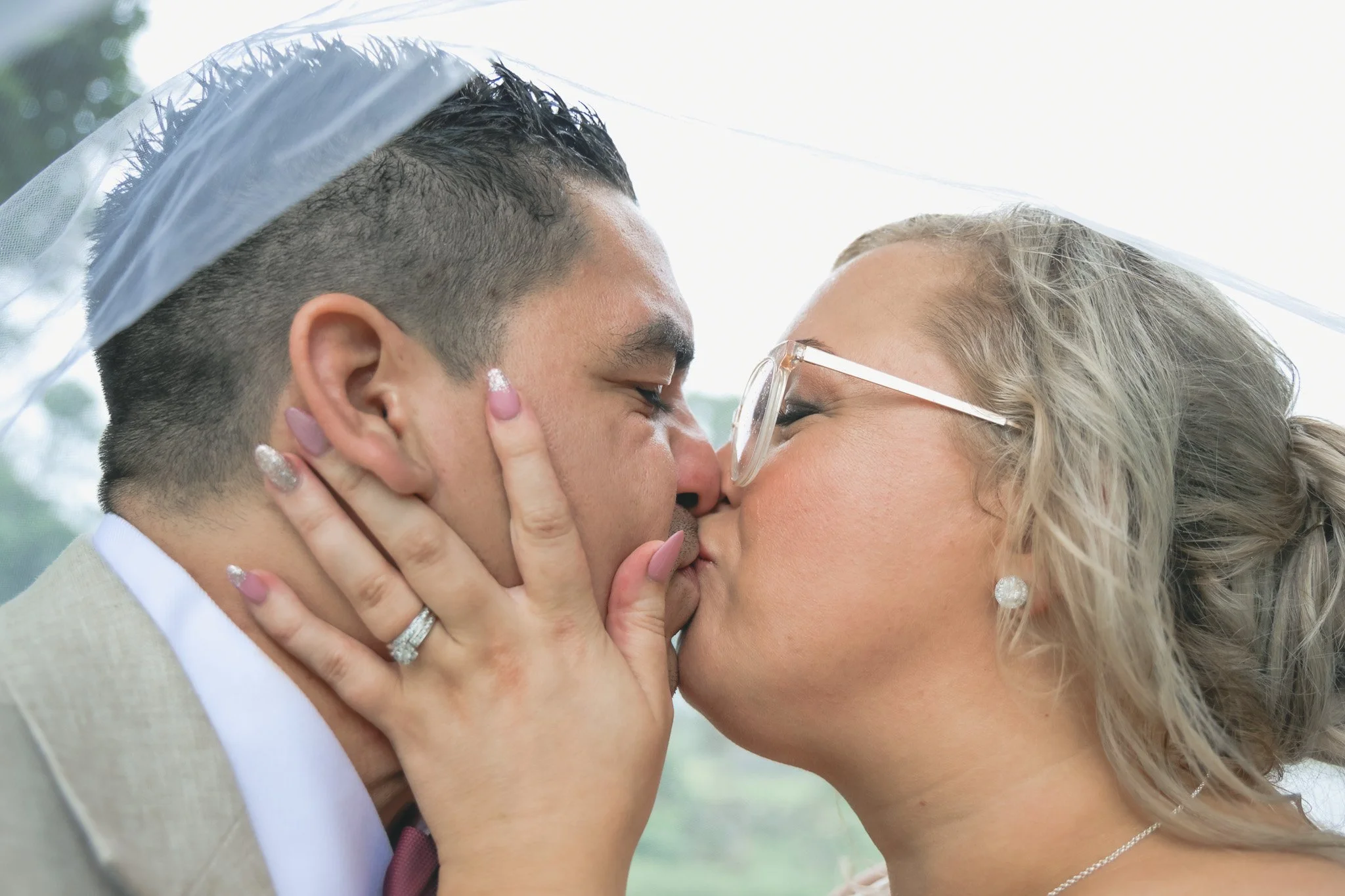 A couple is sharing a kiss outdoors, with the woman gently holding the man's face and both their eyes closed.