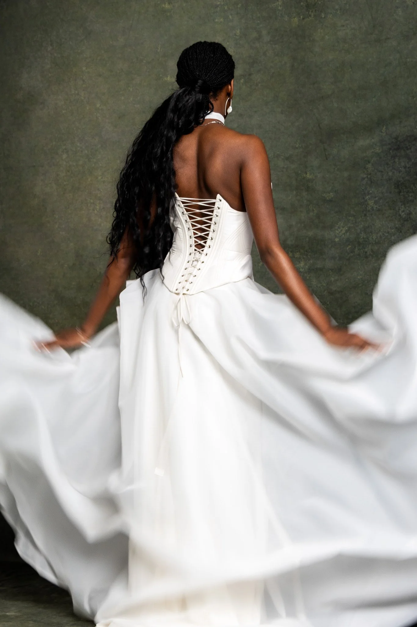 Woman in a white dress spinning around with long dark braids and pearl jewelry, blurred motion of her dress's hem.
