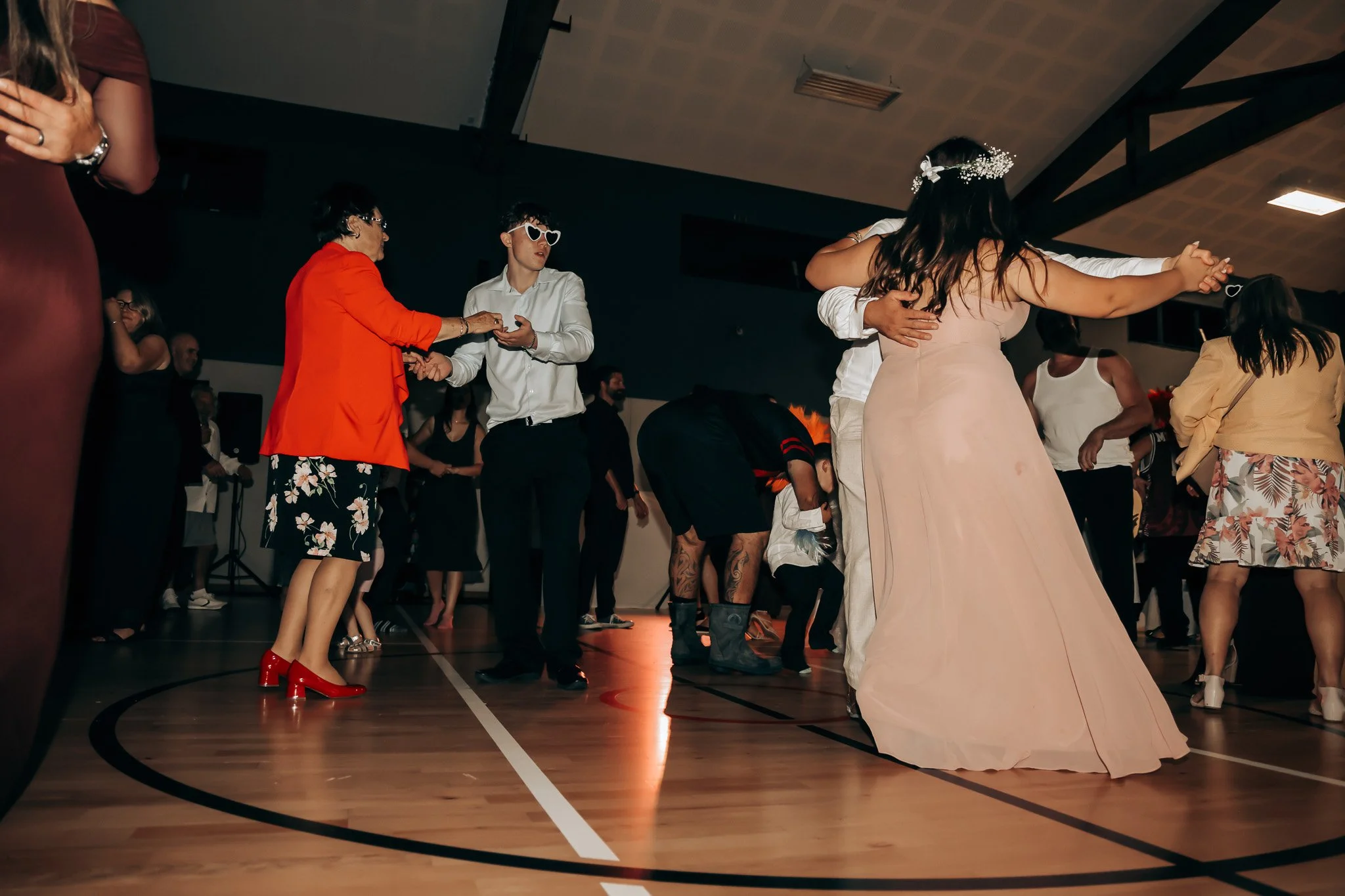 People dancing and socializing in a gymnasium, dressed in formal and festive attire, with some wearing costumes, at a lively event or celebration.