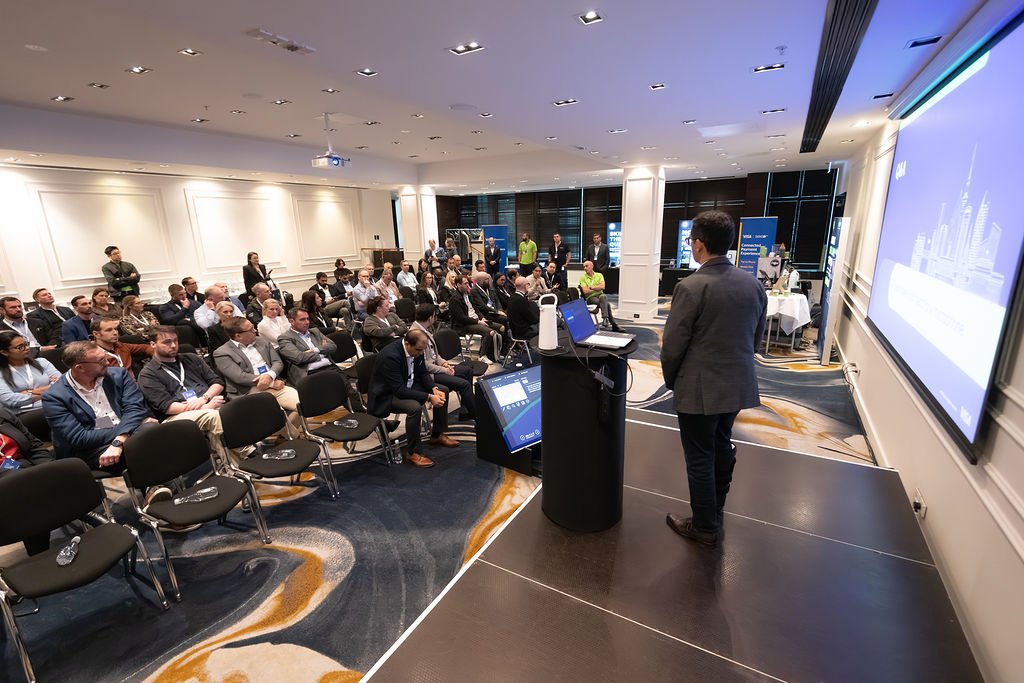 A man in a gray suit presenting to a large audience in a conference room.