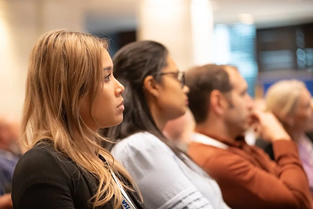 A group of people seated in a conference or seminar, attentively listening to a speaker.