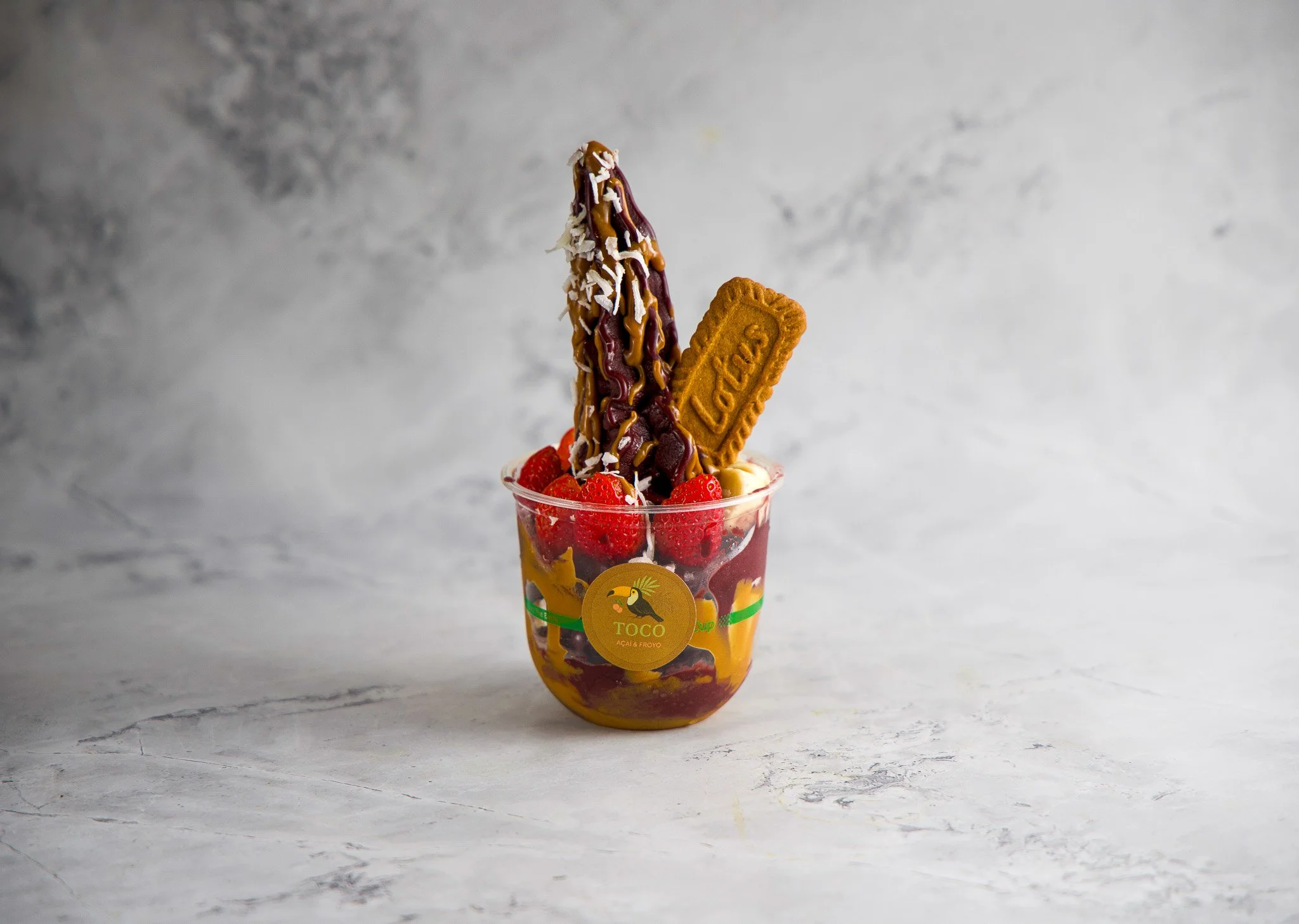 A cup filled with strawberries, a cookie, and a chocolate-covered banana with coconut shavings and sauce drizzled on top.