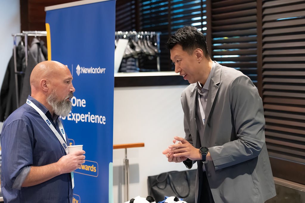 Two men having a conversation at a professional event, with a blue Newland NPT banner in the background.