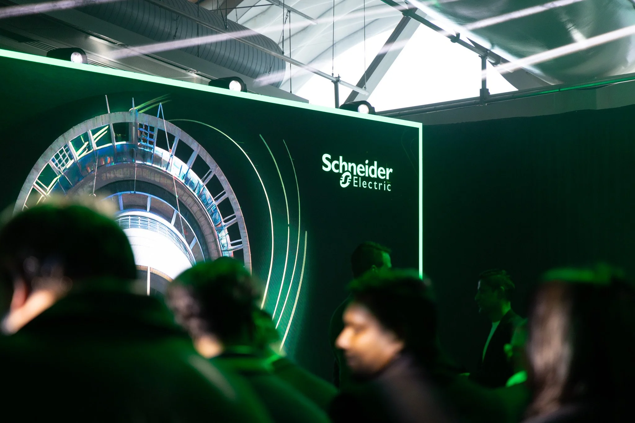 A large display screen with the logo 'Schneider Electric' at an event or conference, with a modern, industrial design featuring neon green lighting and a audience in the foreground.