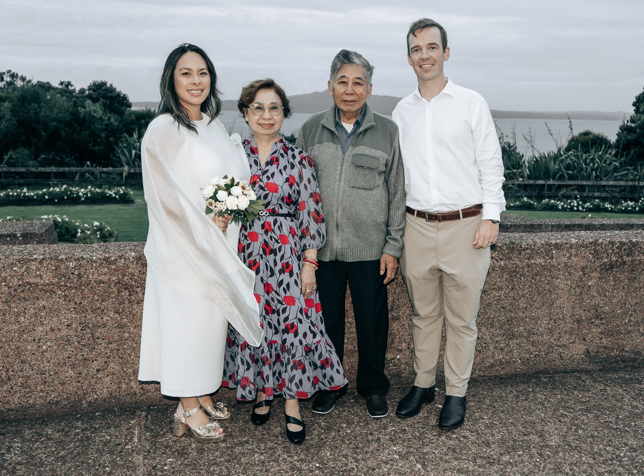 A diverse group of five people standing outdoors, smiling, with a lake and trees in the background on a cloudy day.