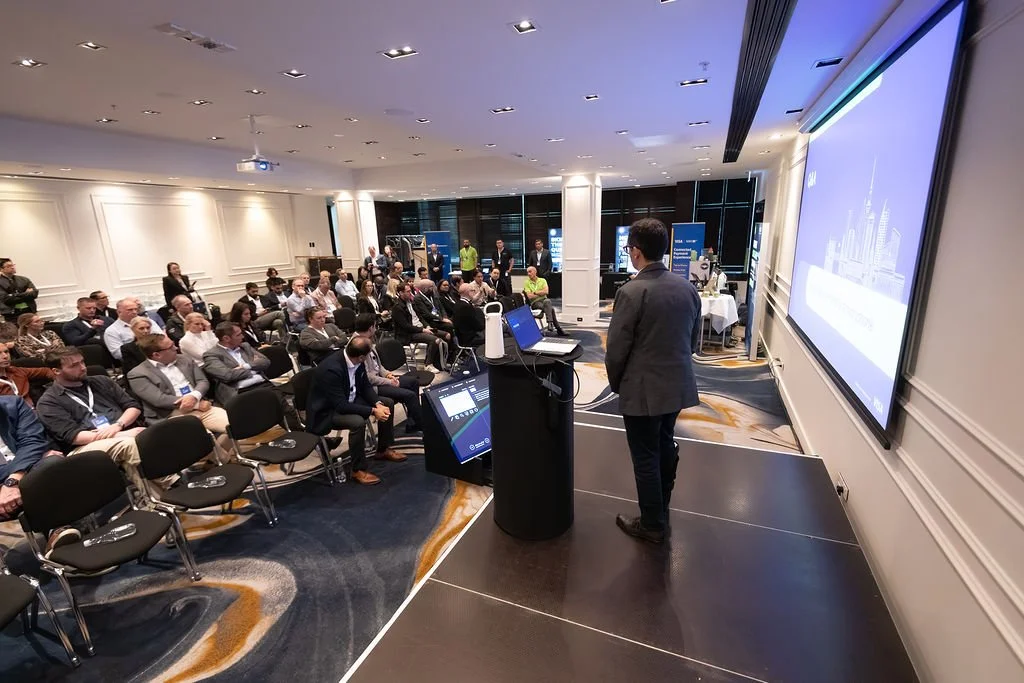 Business conference with a speaker presenting to an audience in a hotel conference room.