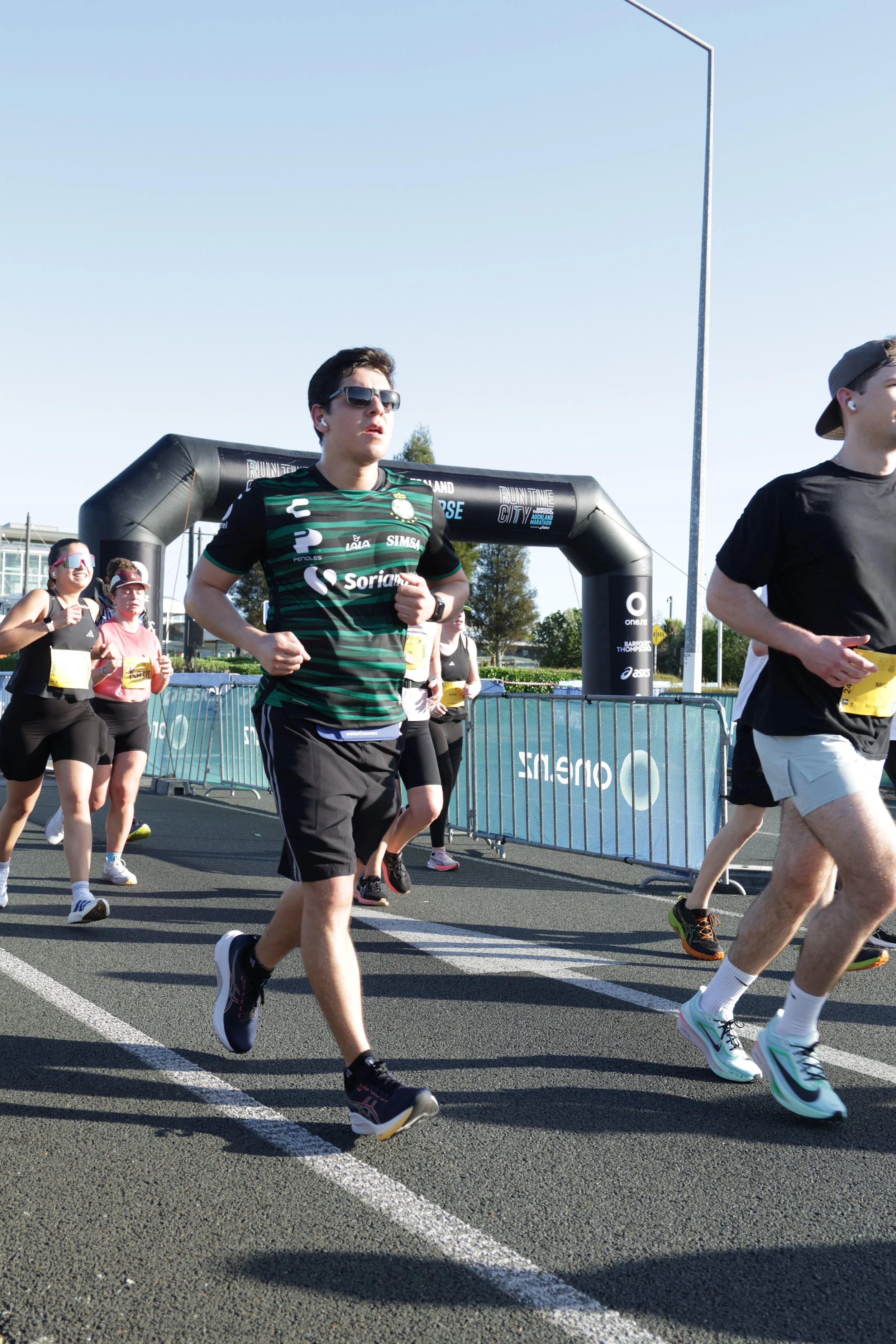 Group of people running in a marathon race on a sunny day, with an inflatable arch in the background and a blue sky overhead.