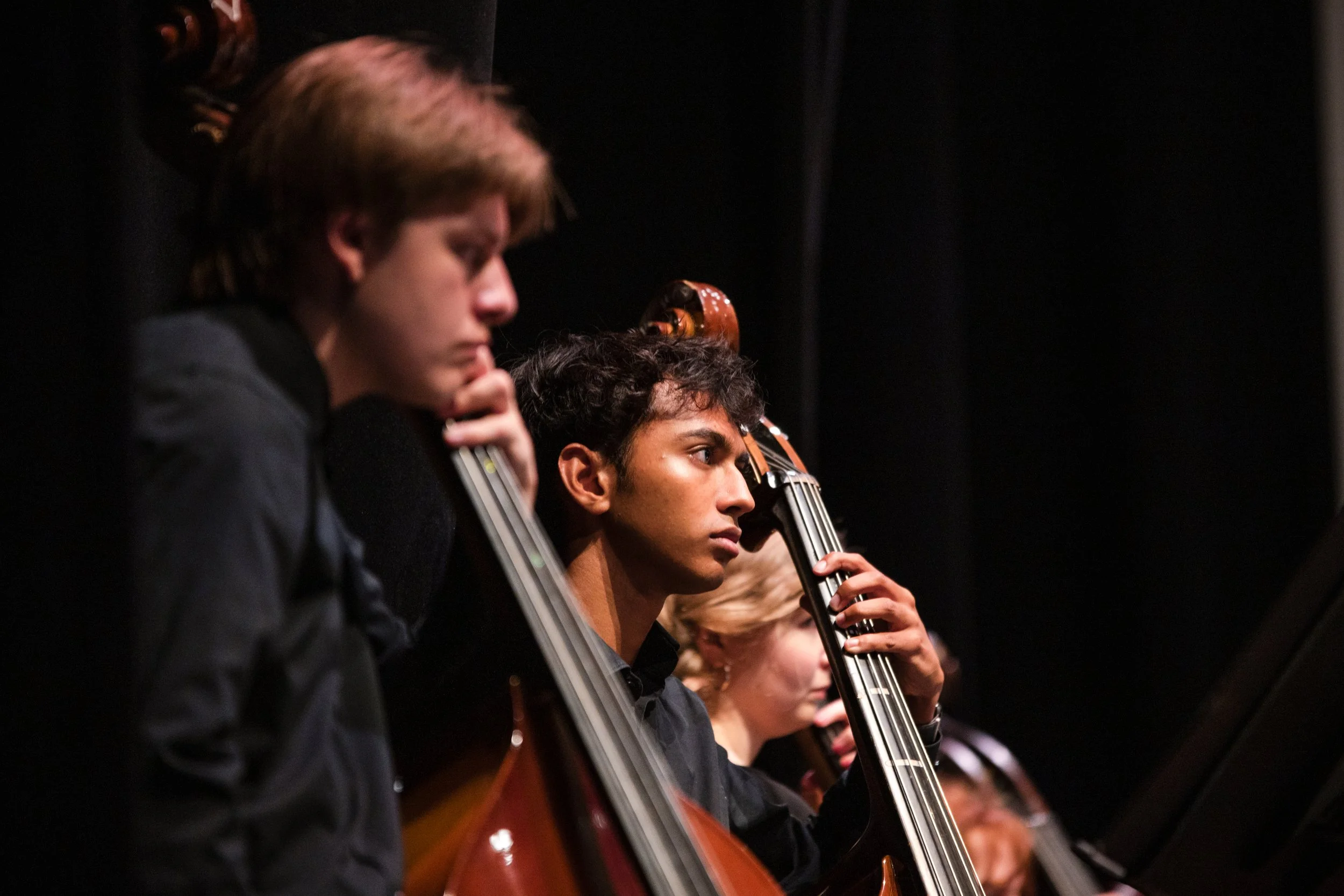 A group of young musicians playing string instruments, likely violins or violas, on stage during a performance, with a focus on their concentration and skill.