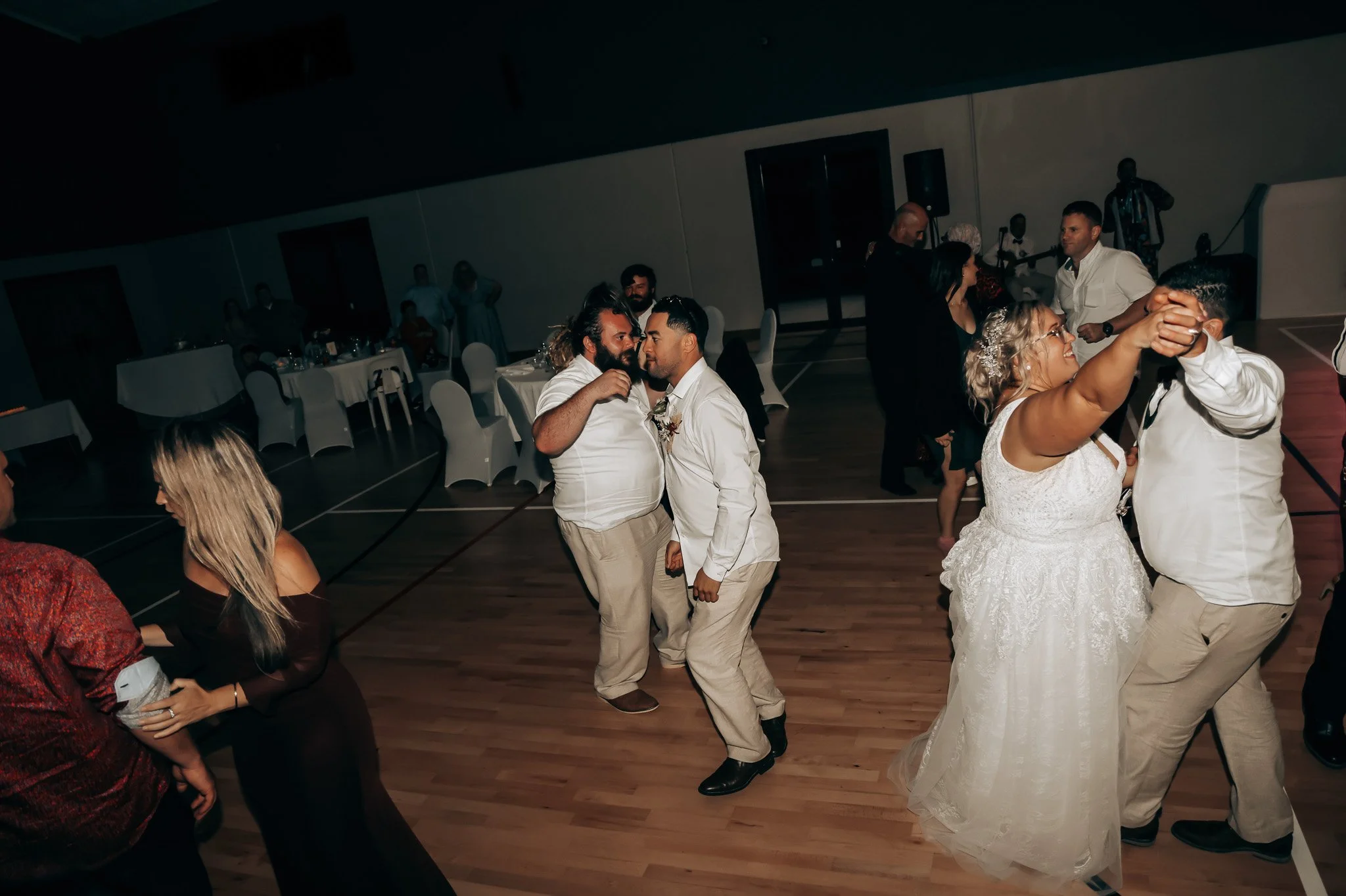 People dancing at a wedding reception with tables, chairs, and live band in the background.