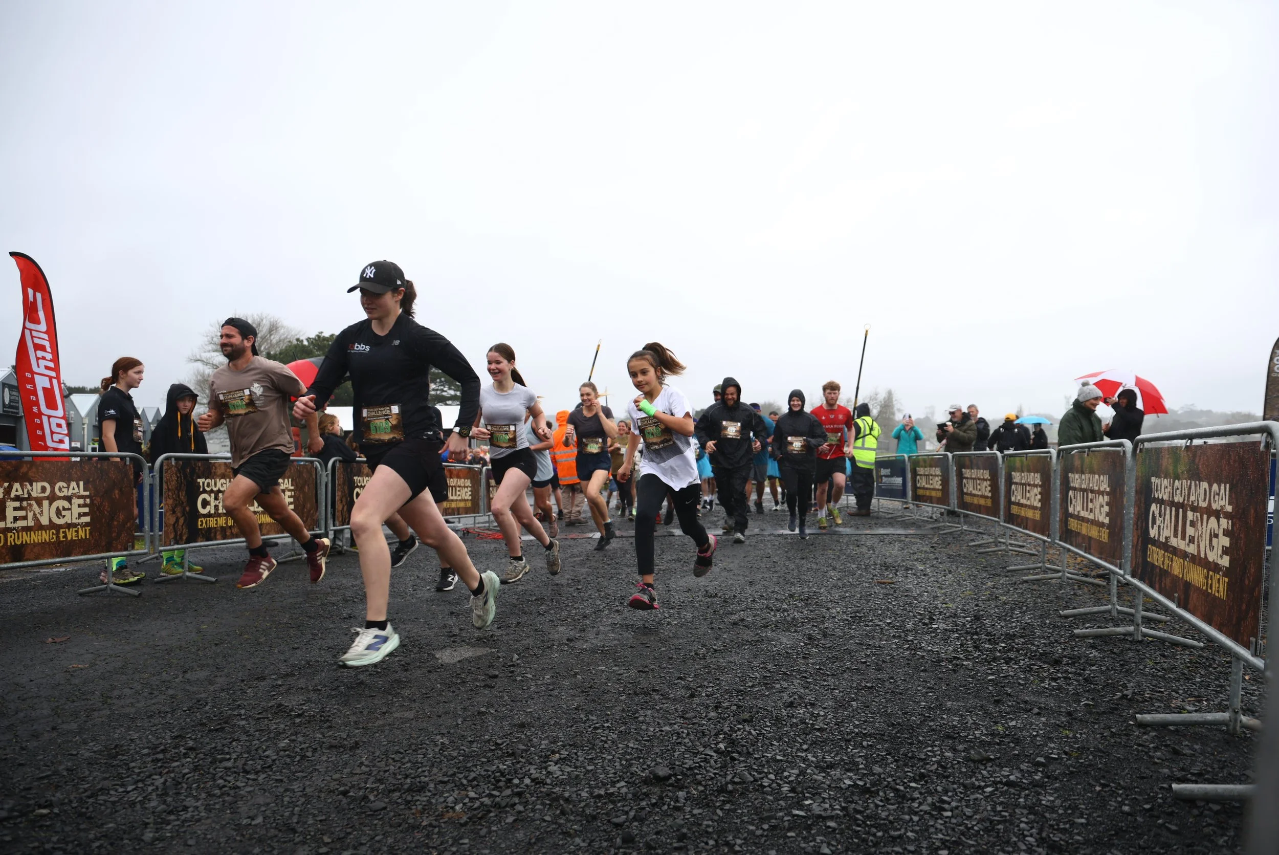 People running in a race event outdoors on a cloudy day, with some spectators and event volunteers in the background.
