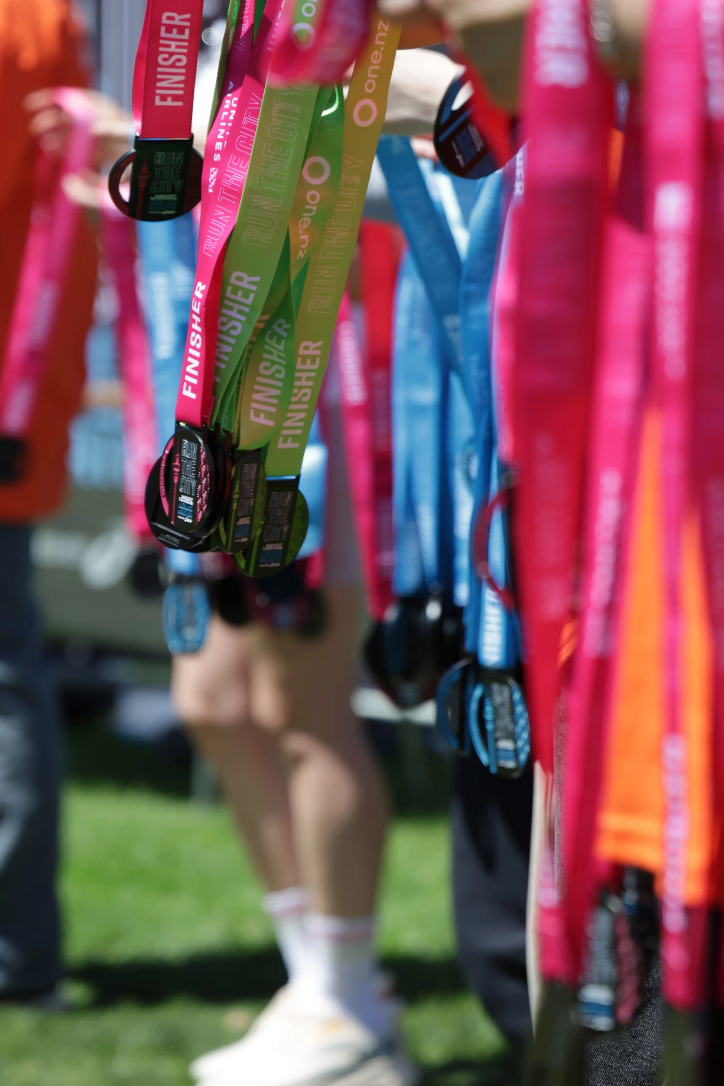 Close-up of race medals hanging on a rack with runners and grass in the background.
