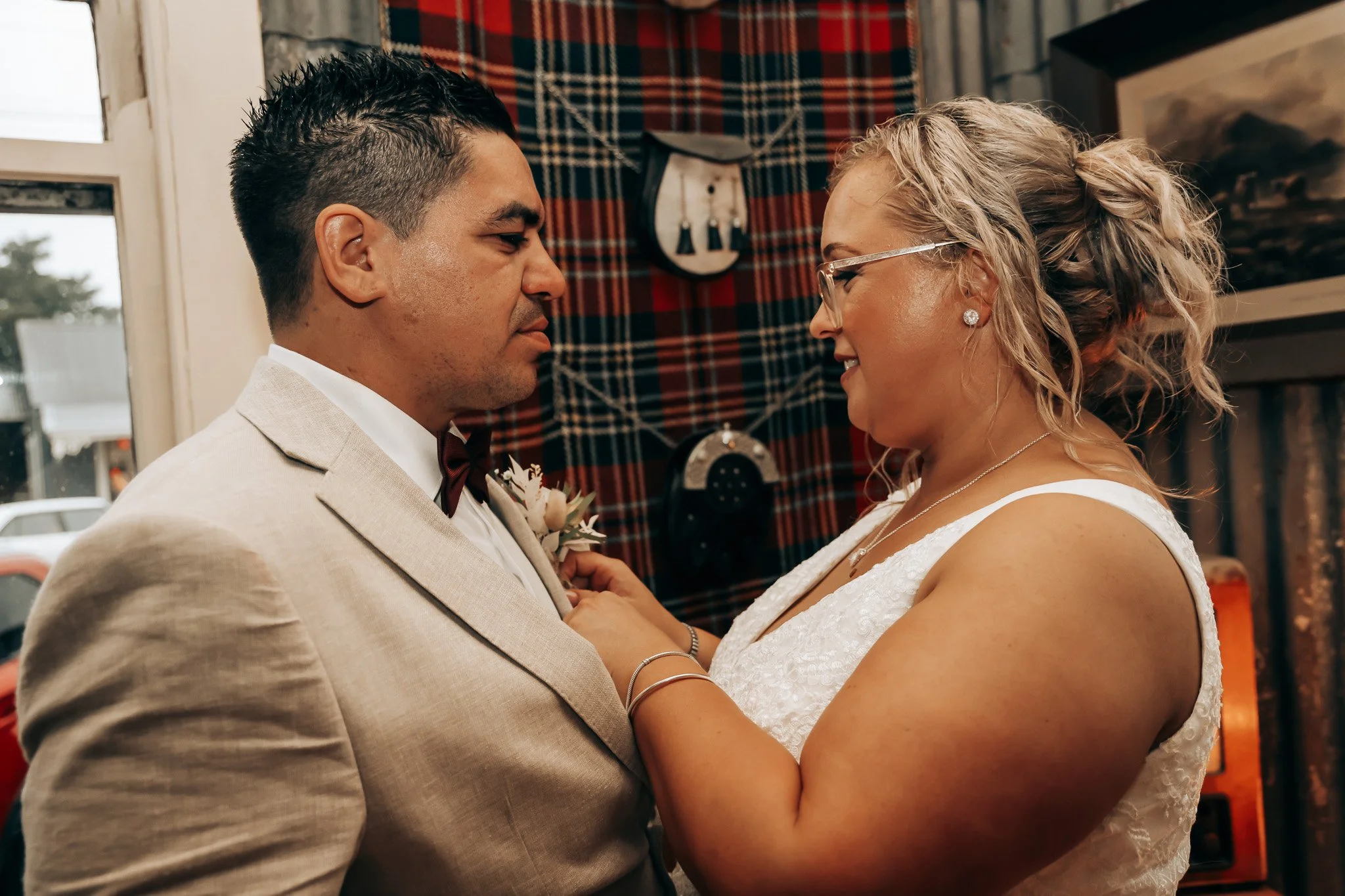 A bride and groom sharing a dance indoors, close in an intimate moment, with a rustic background featuring a plaid curtain and decor.