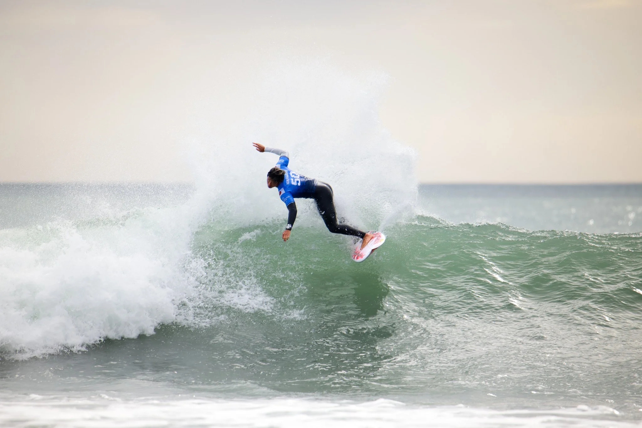 A person surfing on a wave in the ocean, wearing a blue and black wetsuit.