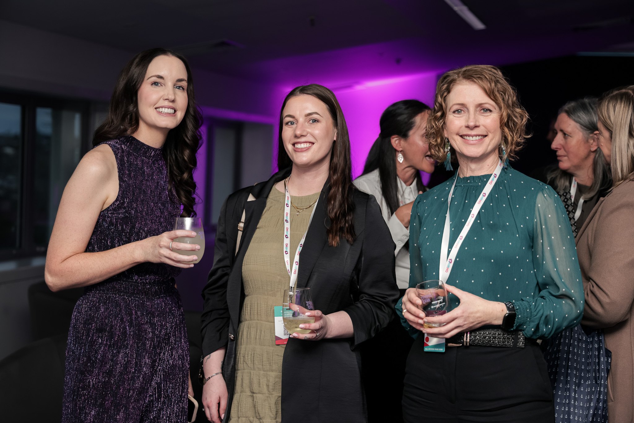 Group of women at a social event, holding drinks and wearing conference badges.