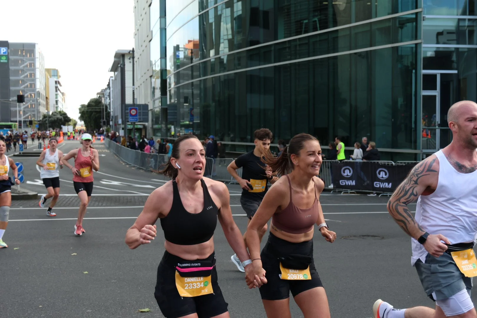 Marathon runners participating in a road race in an urban area with modern glass buildings and city infrastructure.