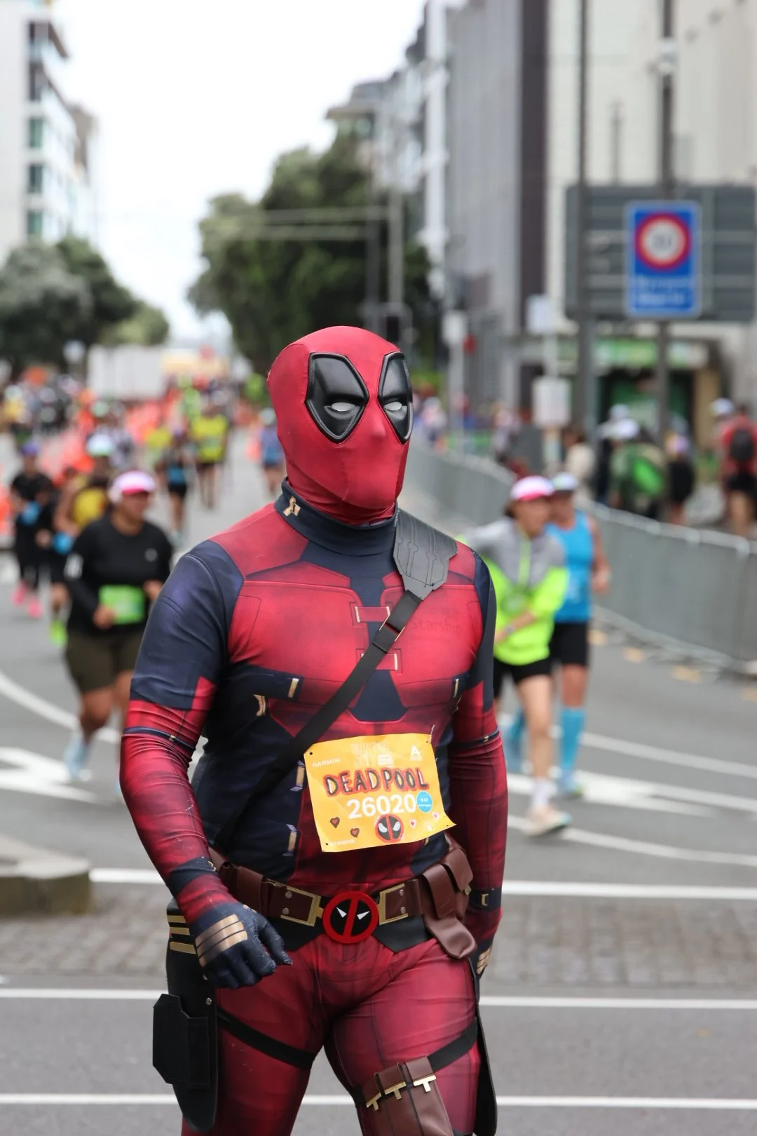 A person dressed as Deadpool at a marathon, surrounded by other runners on a city street.