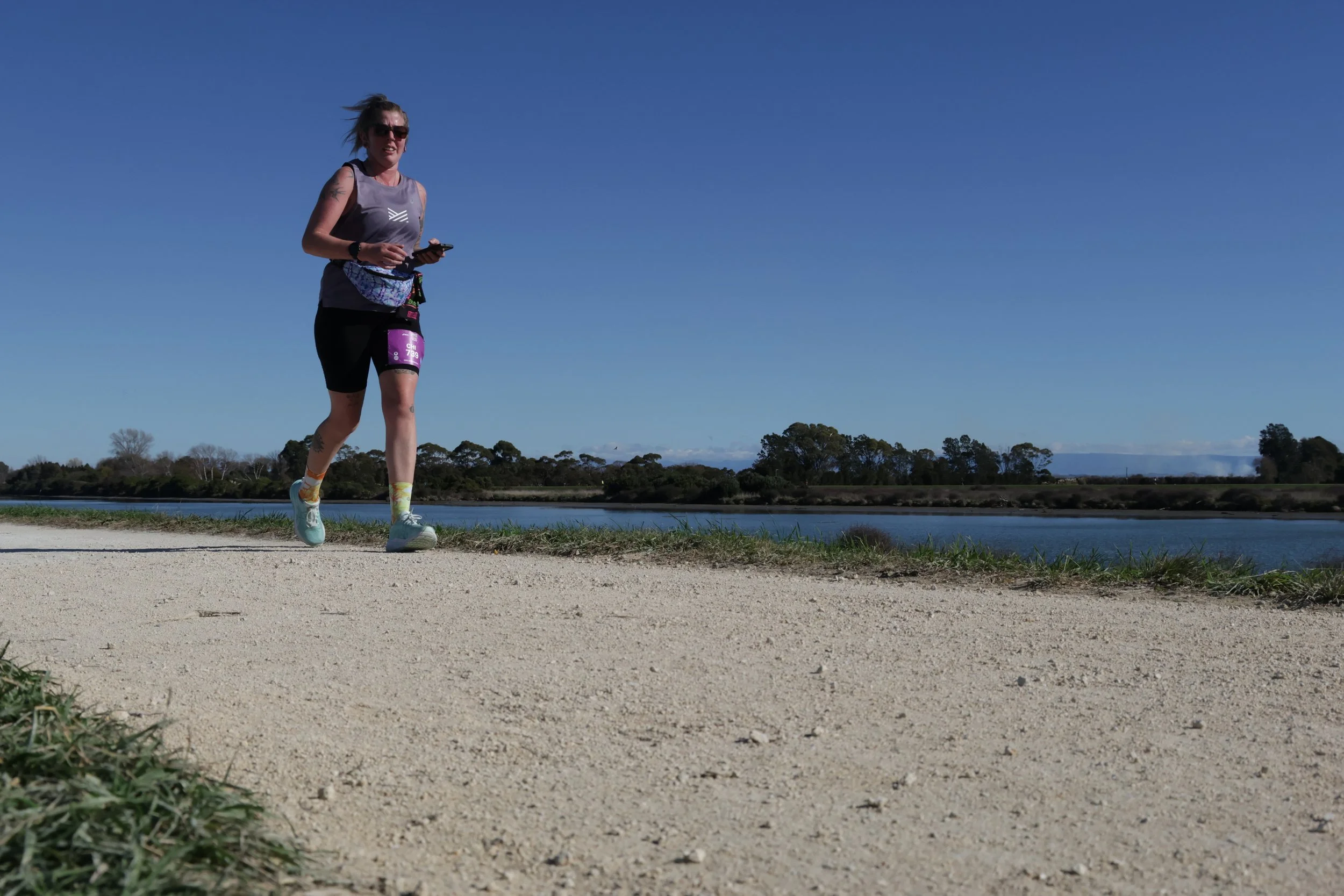 A woman in athletic clothing jogging along a path near a body of water on a clear day.