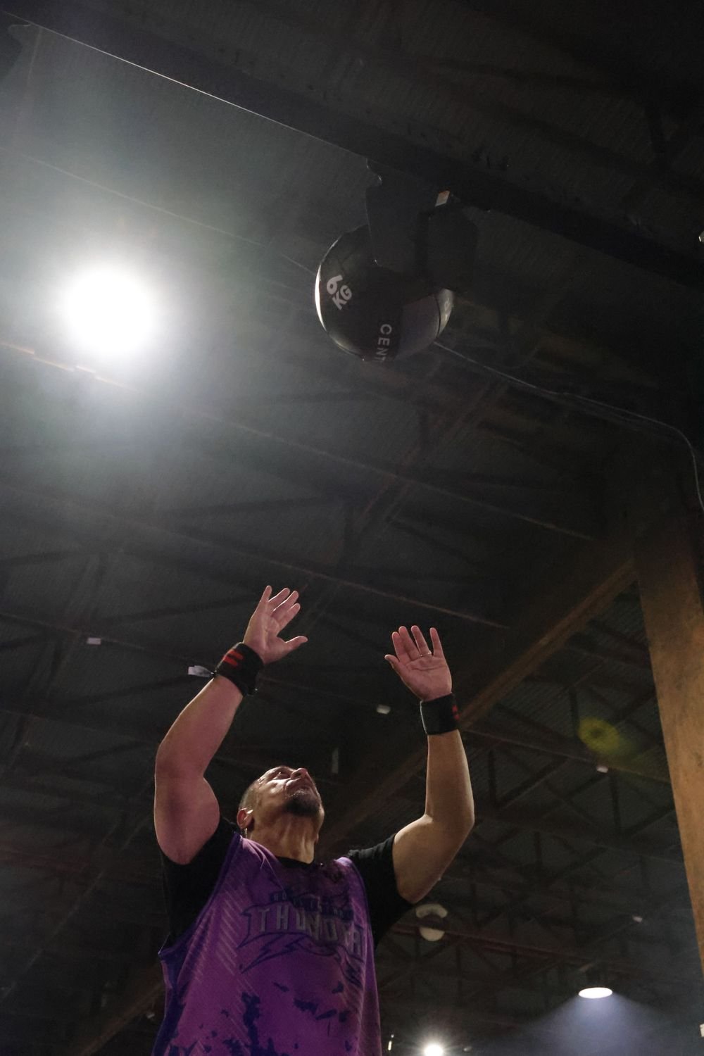 A person playing basketball inside a gym with a ceiling and a large overhead light visible.