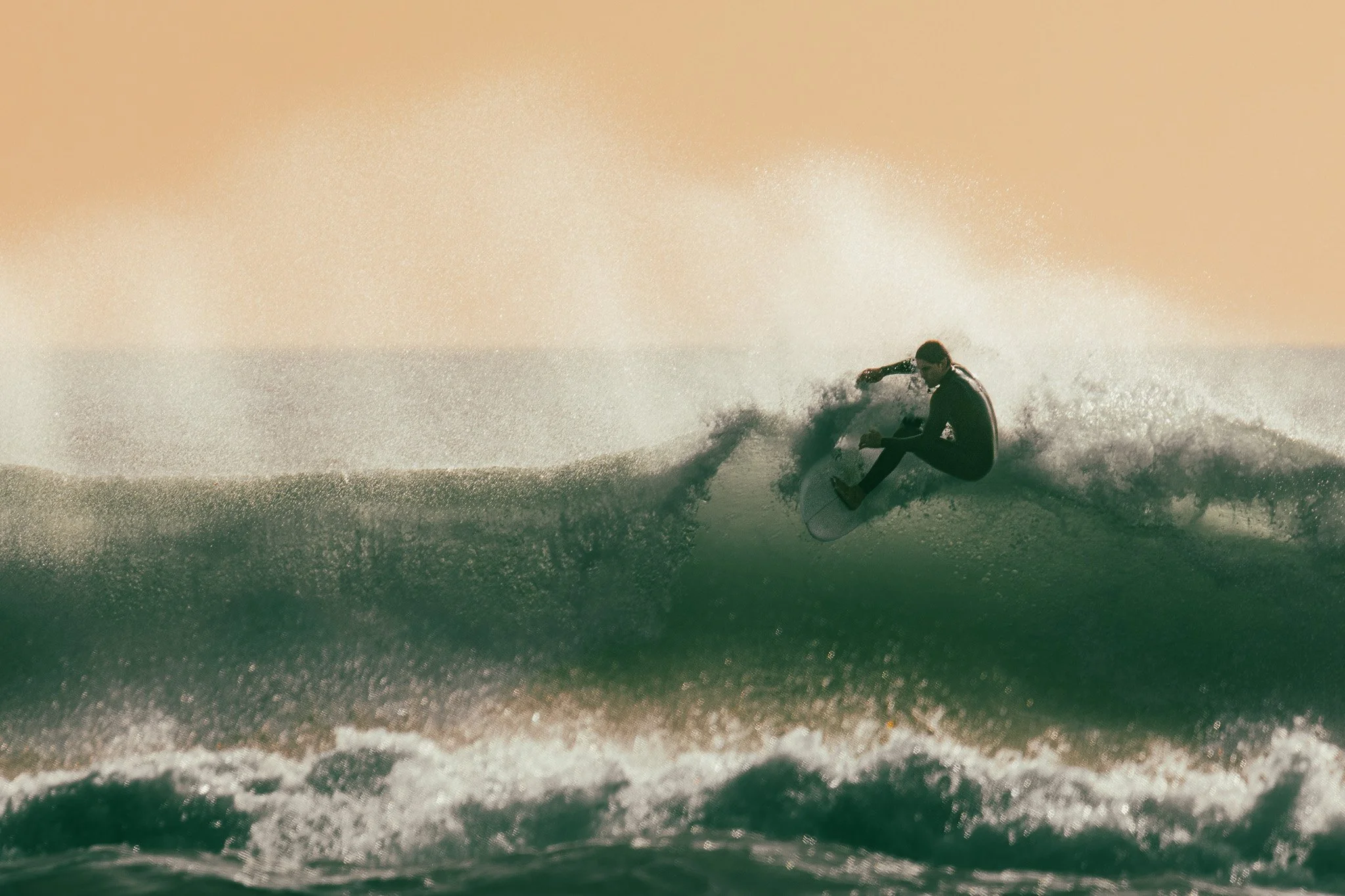 A person surfing on a wave at sunset with a warm, orange sky.