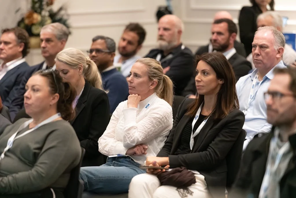 A group of people attending a conference or seminar, seated in rows, with some taking notes and others listening attentively.