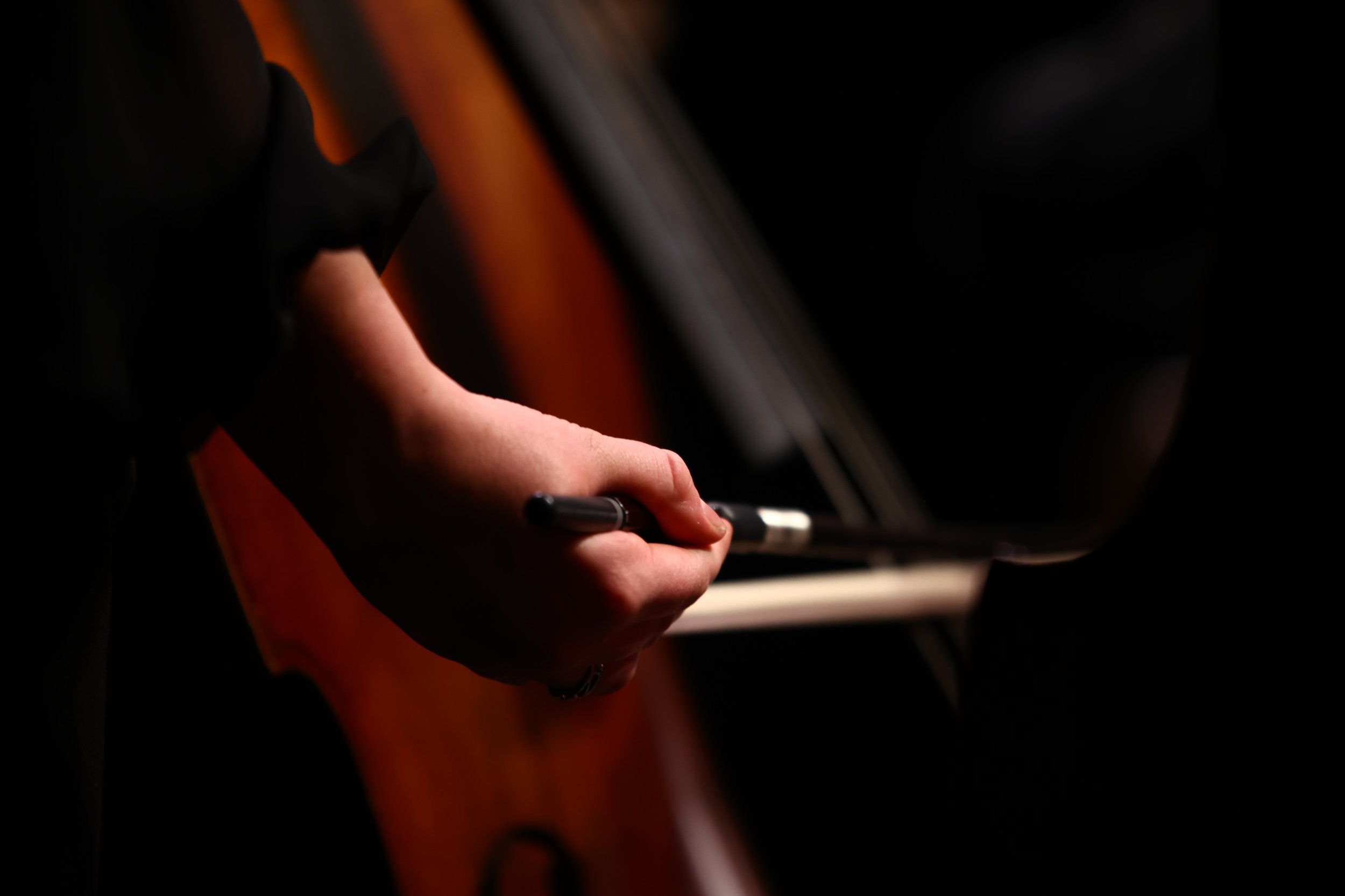 Close-up of a person's hand holding a pen, with the arm resting on a surface against a dark background.