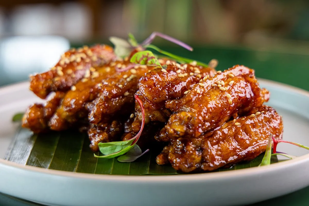 Close-up of glazed chicken wings garnished with microgreens on a leaf on a white plate.