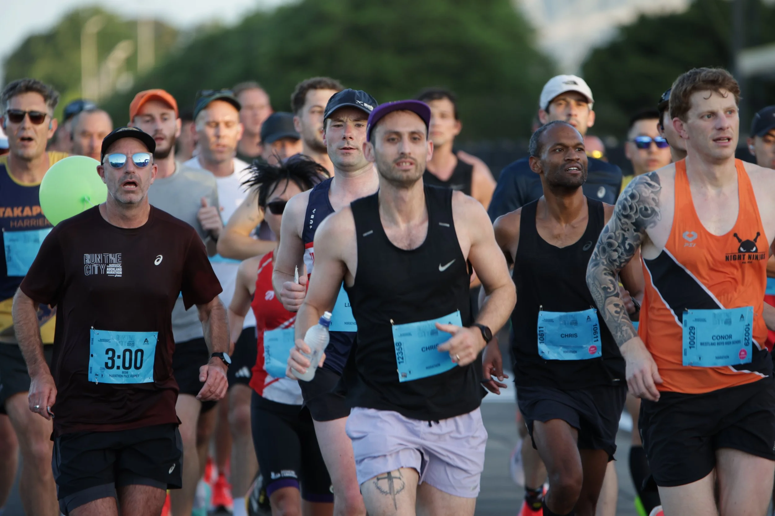 A group of people participating in a marathon or running event, wearing athletic clothing and race bibs, running outdoors during daytime.