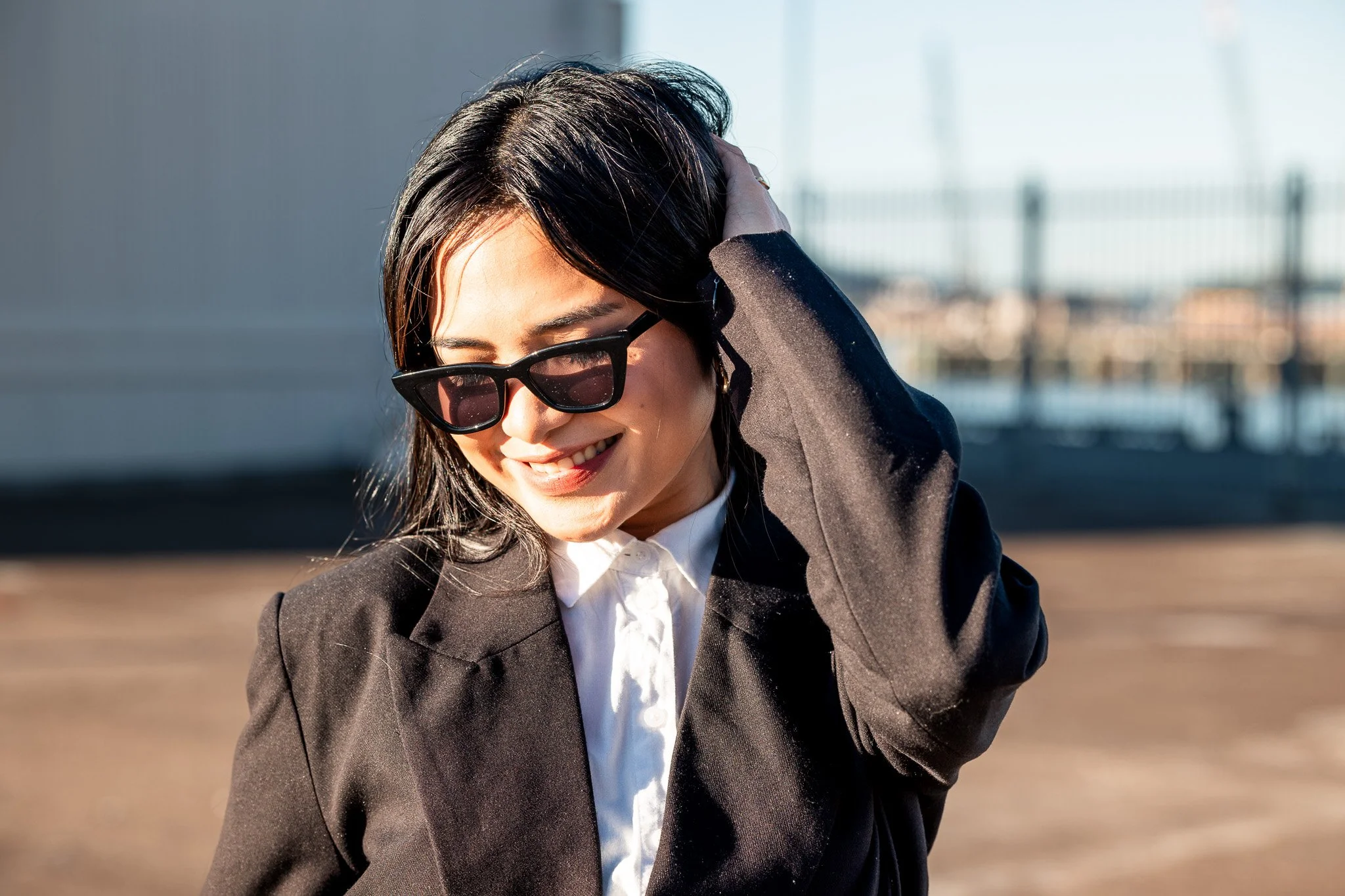 A woman wearing sunglasses and a black blazer smiling outdoors.