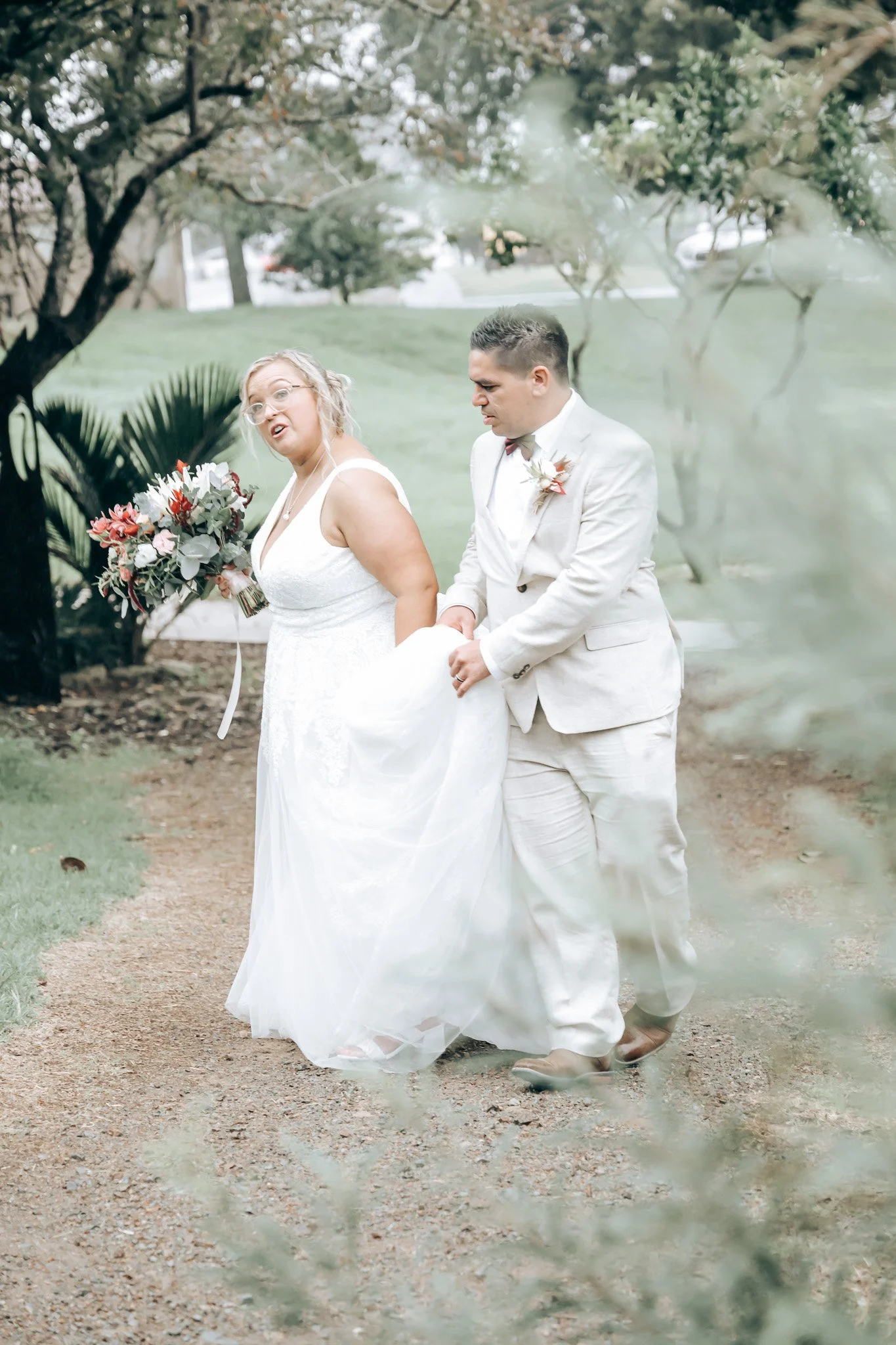 A bride and groom holding hands during their wedding ceremony outdoors, surrounded by green trees and foliage.