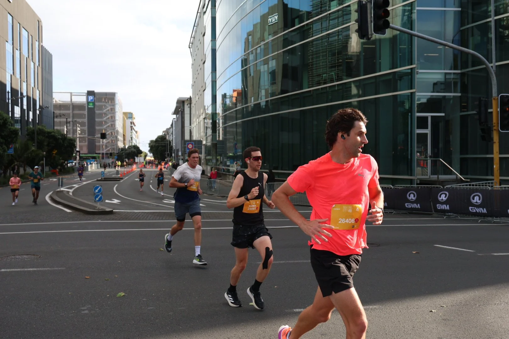 People running in a road race through a city street with modern glass buildings in the background.