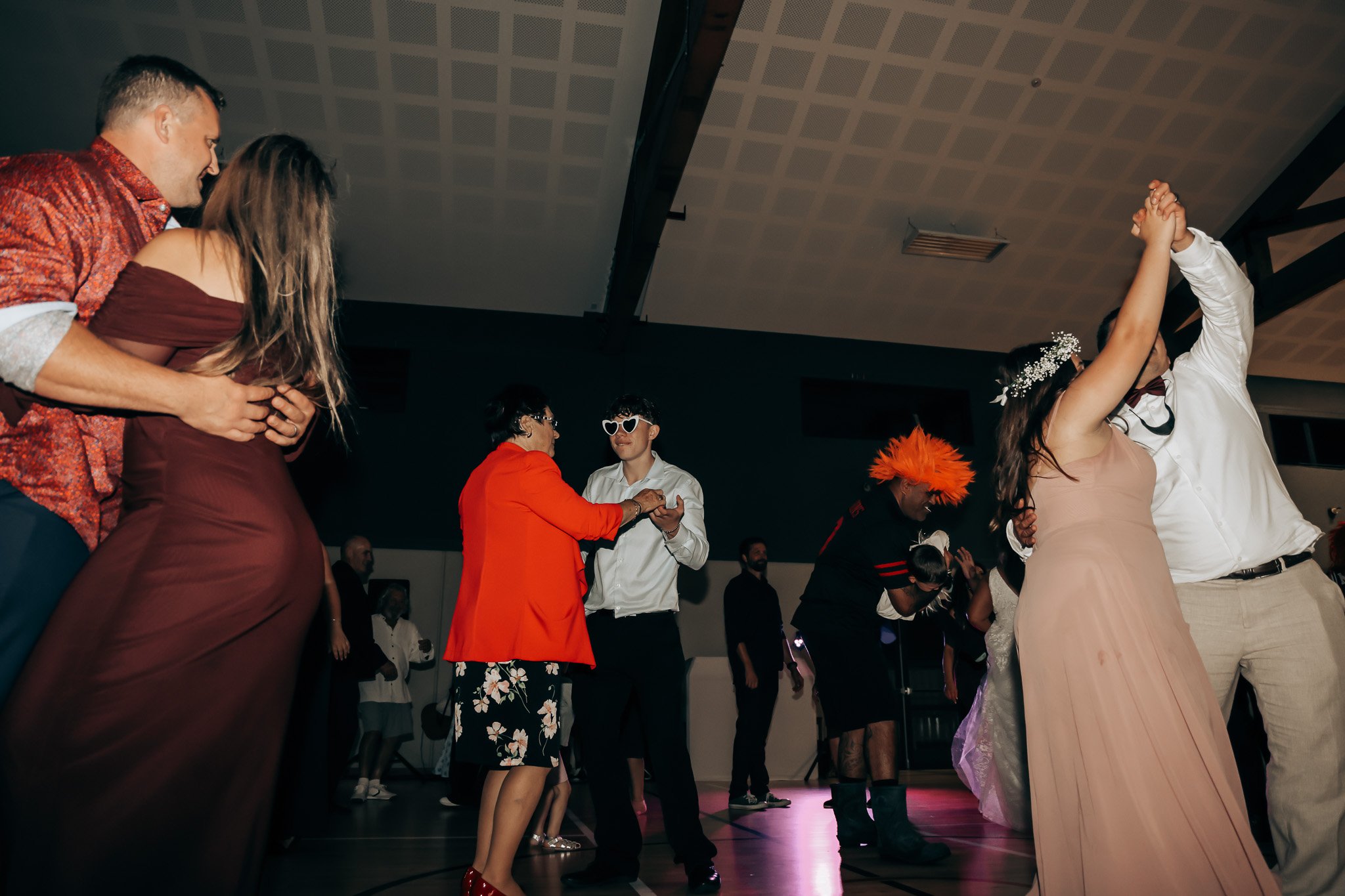 People dancing and socializing in a dimly lit indoor venue, some wearing costumes and accessories like heart-shaped sunglasses and floral headpieces.