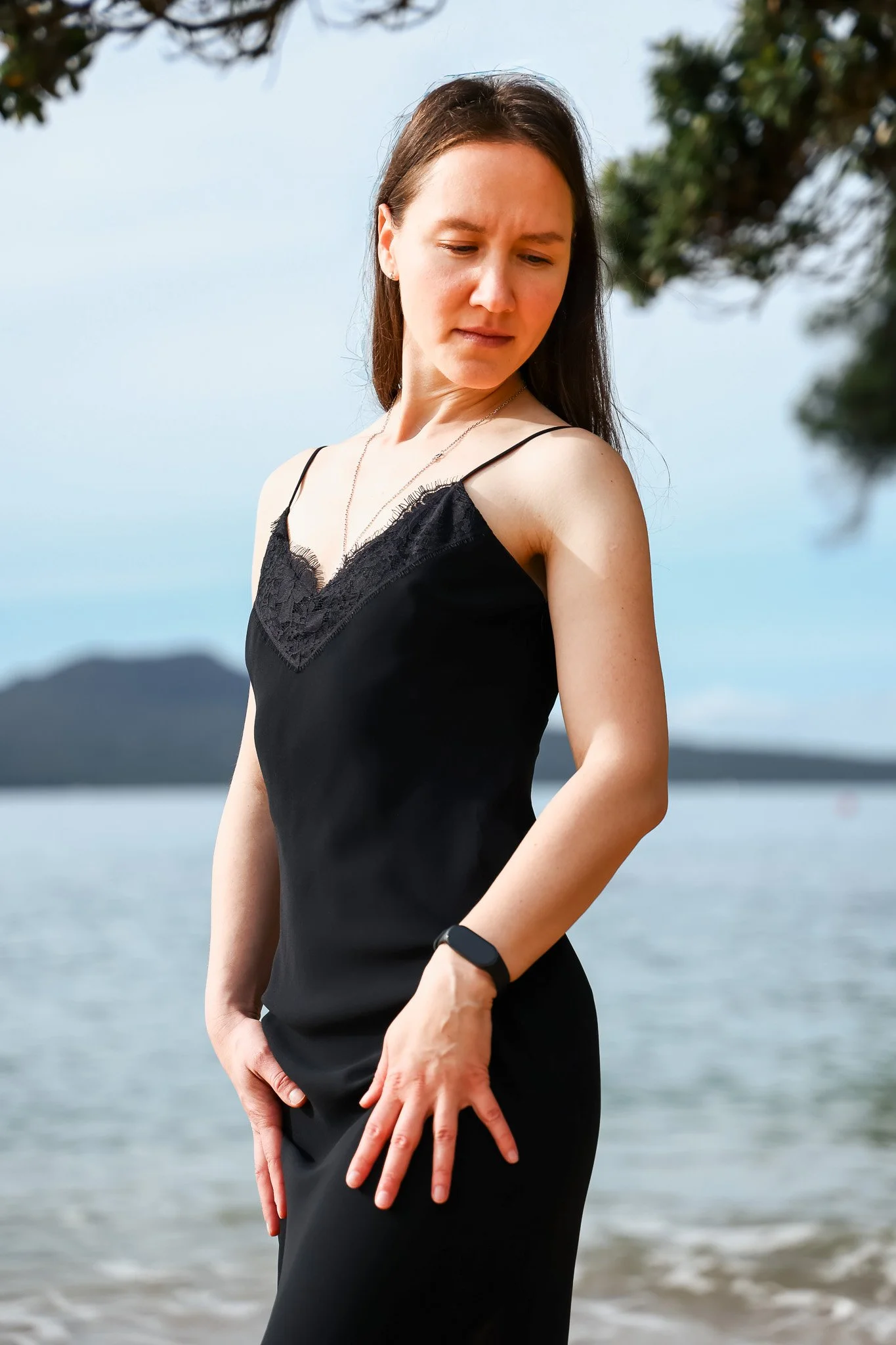 Woman in a black dress standing by the water with mountains in the background