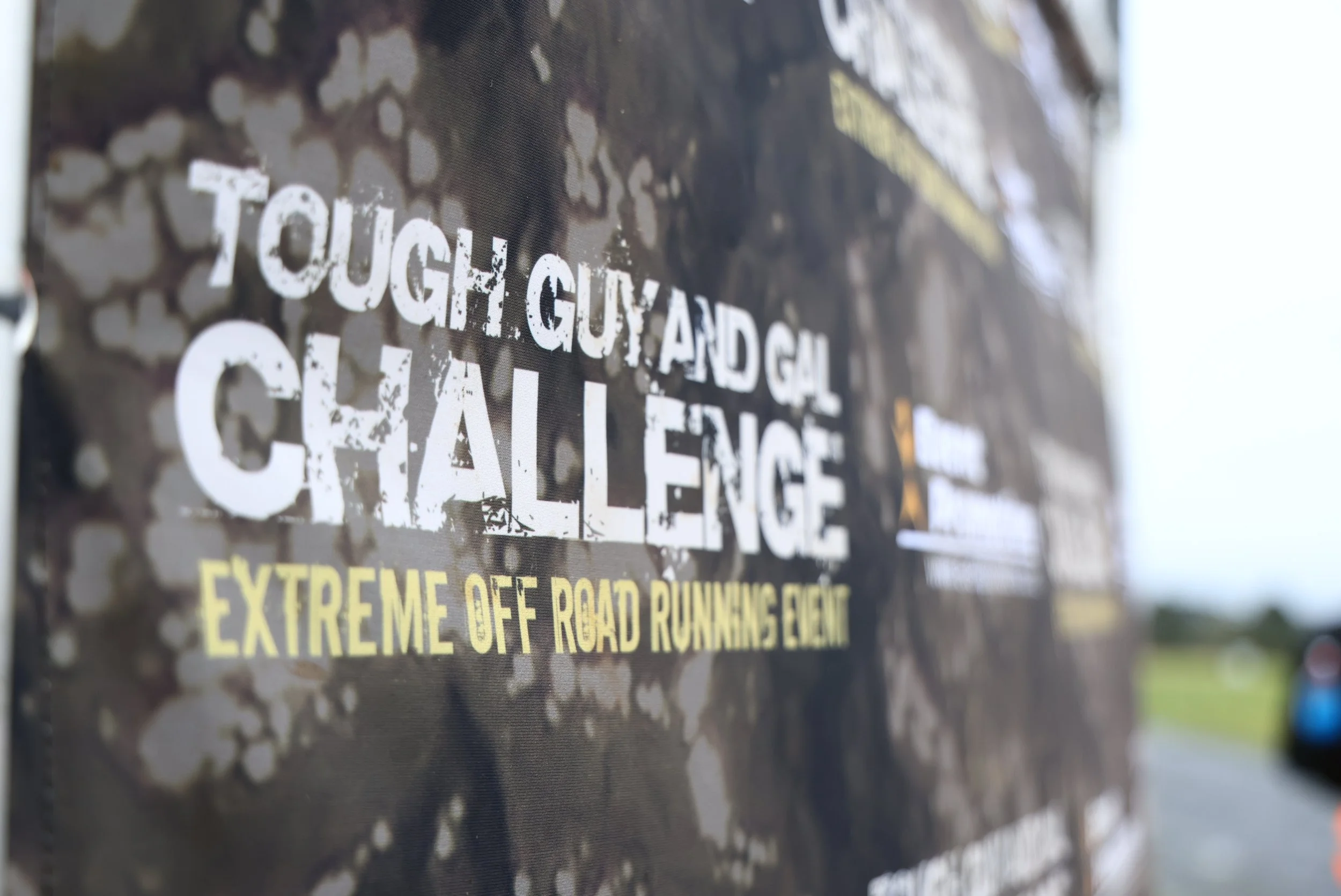 Close-up of a warning or caution sign with white and yellow text on a black background, partially visible, warning about extreme off-road running event.